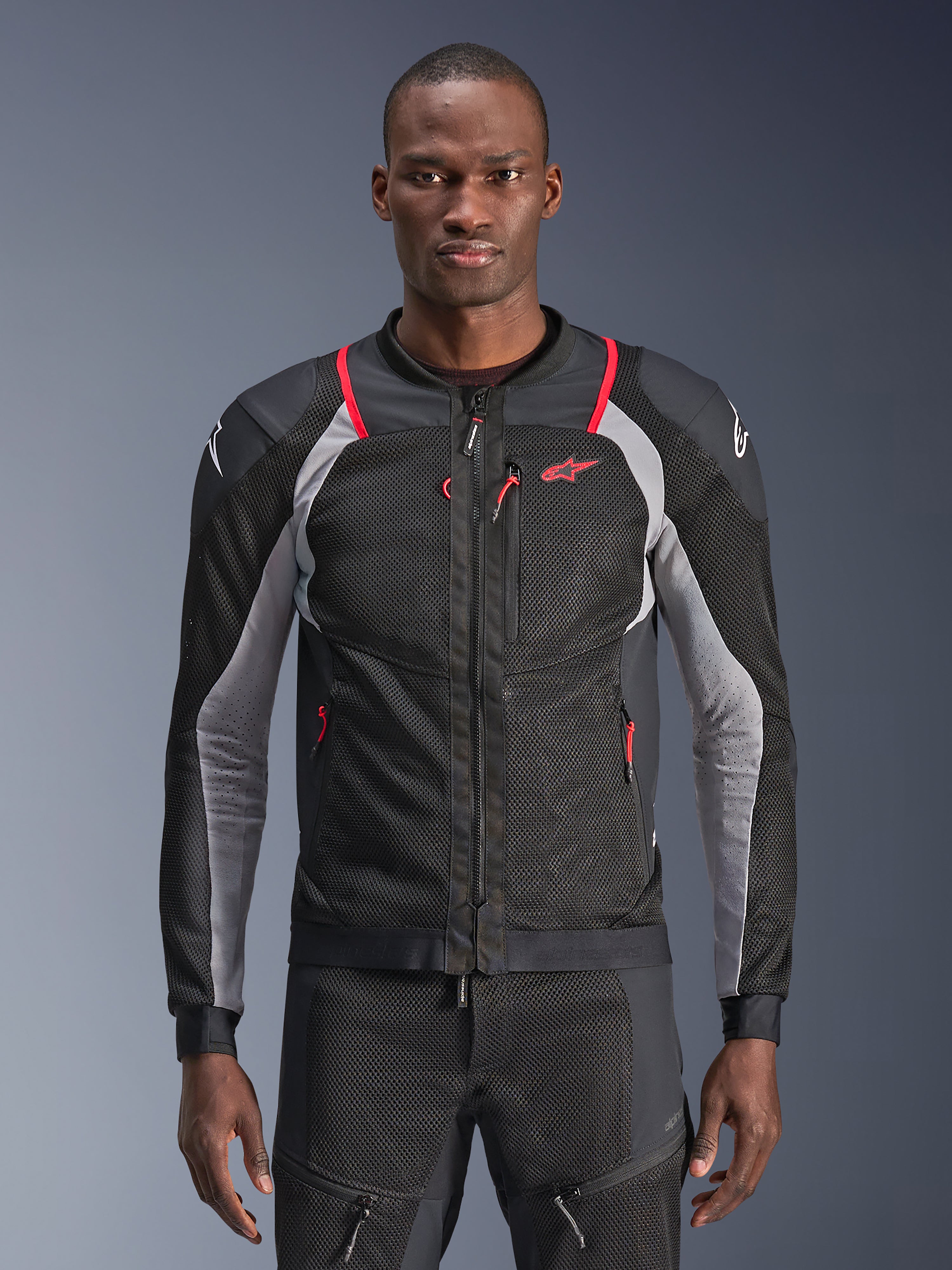 Alpinestars Troop-Air Pro Jacket, czarna i szara z jaskrawoczerwonymi akcentami, prezentowana na modelu, motocyklowa kurtka siatkowa z perforowanymi panelami wentylacyjnymi, czerwone kieszenie na zamek, białe logo na ramionach, techniczna odzież ochronna