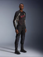 Kurtka Alpinestars Troop-Air, techniczna siatkowa kurtka motocyklowa w kolorach czarnym, popielatym i jasnoczerwonym, prezentowana przez modela z czarnymi spodniami i butami, czerwone logo Alpinestars na piersi, nowoczesna odzież motocyklowa w stylu miejskim.