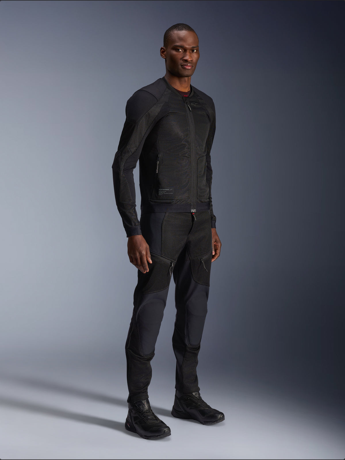 Alpinestars Troop-Air Jacket, czarna, techniczna siatkowa kurtka motocyklowa prezentowana przez modela z pasującymi czarnymi spodniami i butami, lekka konstrukcja z siatki i minimalistyczny miejski design