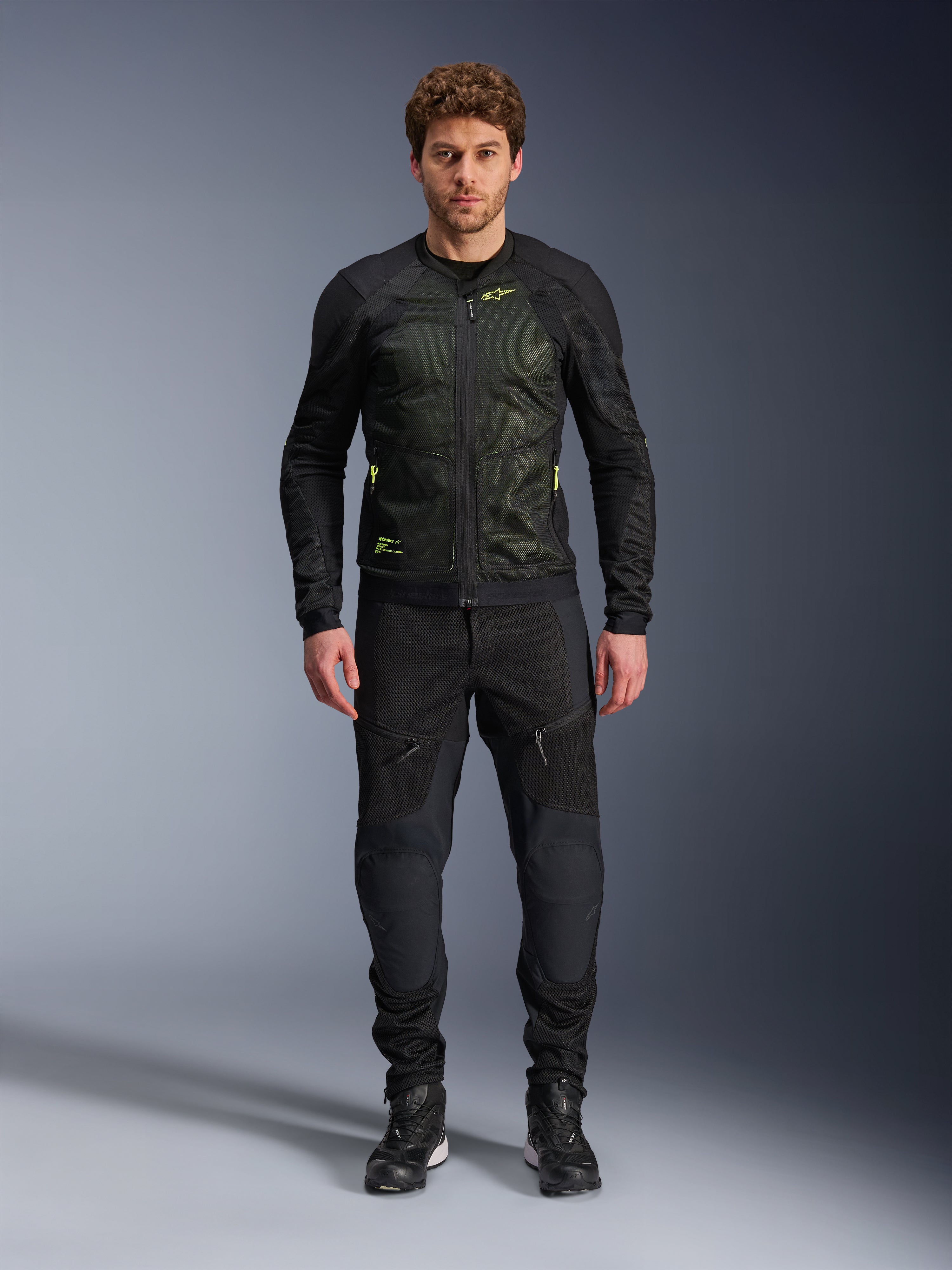 Męski model w kurtce Alpinestars Troop-Air w kolorze Black Yellow Fluo, z technicznymi panelami z siatki i jaskrawożółtymi akcentami, w zestawieniu z czarnymi spodniami i butami motocyklowymi, nowoczesna odzież motocyklowa na ciepłe dni