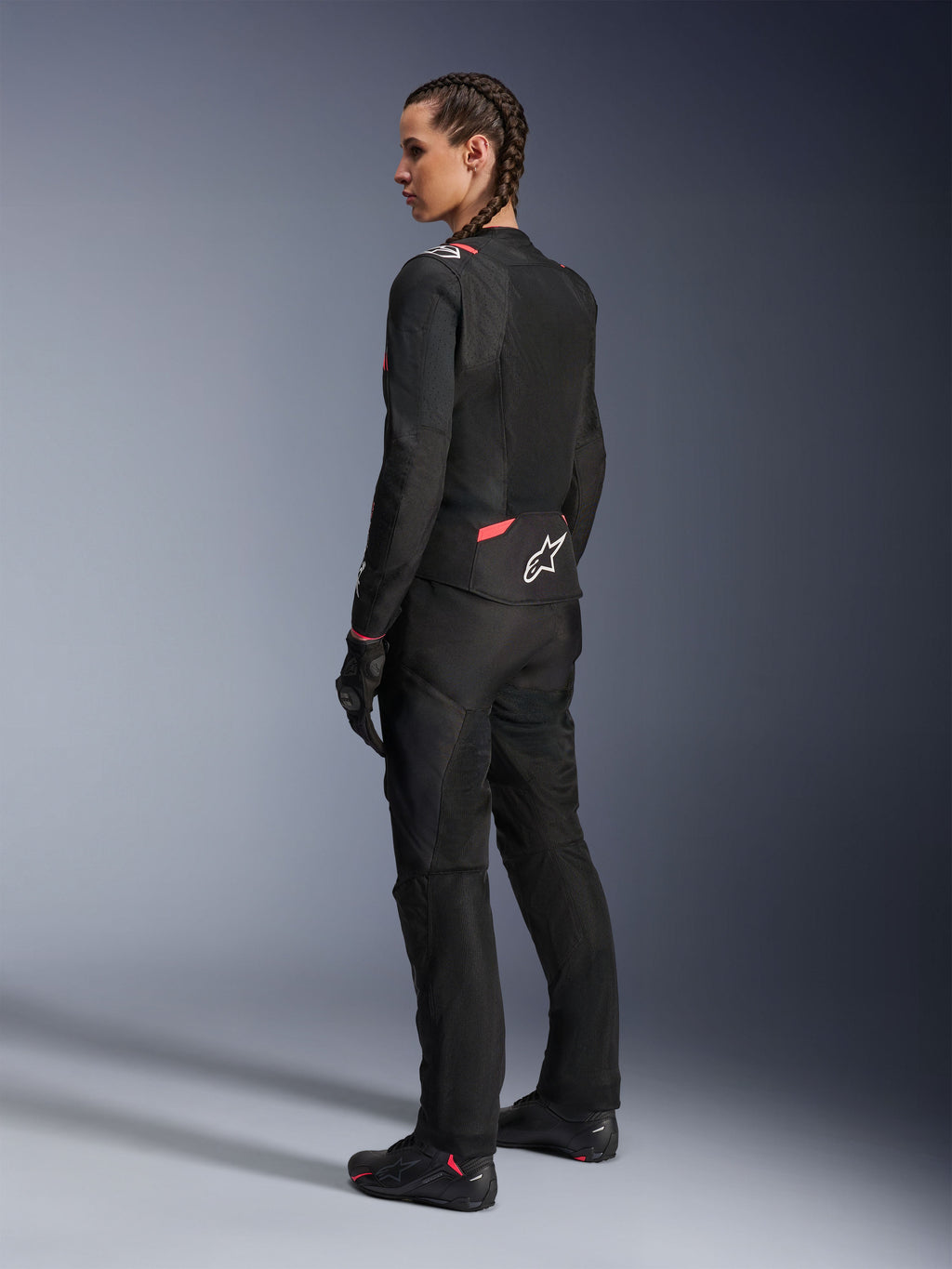 Alpinestars Stella T-Sps Air v2 Jacket, damska tekstylna kurtka motocyklowa, czarna z różowymi akcentami Diva Pink, widok z boku i od tyłu, duże panele z siatki zapewniające przepływ powietrza, białe logo z gwiazdą na plecach, noszona z dopasowanymi czarnymi spodniami, rękawicami i butami.