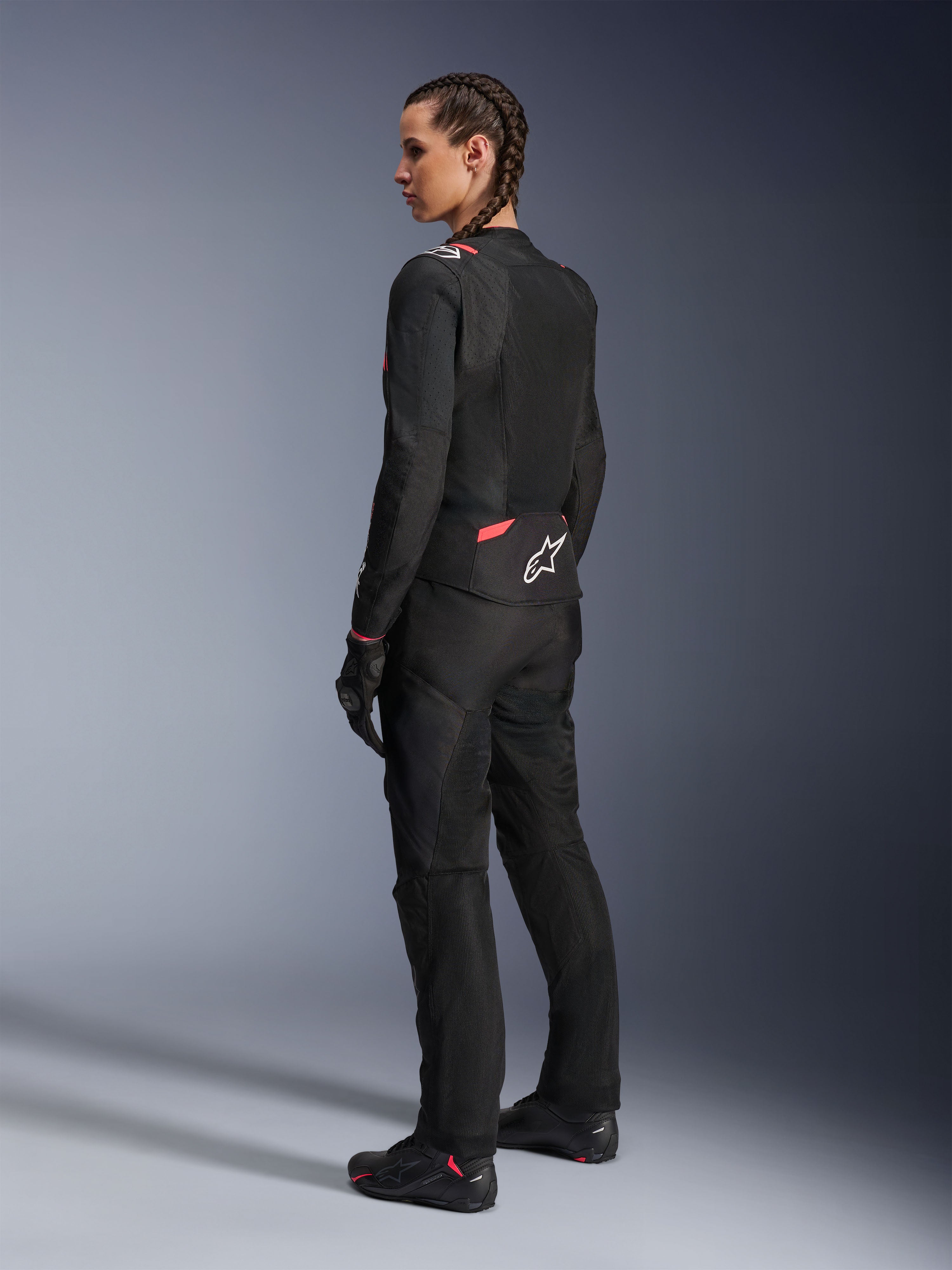 Alpinestars Stella T-Sps Air v2 Jacket, damska tekstylna kurtka motocyklowa, czarna z różowymi akcentami Diva Pink, widok z boku i od tyłu, duże panele z siatki zapewniające przepływ powietrza, białe logo z gwiazdą na plecach, noszona z dopasowanymi czarnymi spodniami, rękawicami i butami.