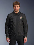 Alpinestars Ignite Air Jacket, czarna kurtka motocyklowa, tradycyjny kołnierzyk koszulowy, pomarańczowo-białe logo „A” na piersi, mankiety w beżowe paski z białym logo gwiazdy, nowoczesna miejska odzież motocyklowa
