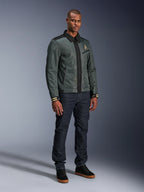 Alpinestars Ignite Air Jacket, Urban Gray Black Blue, miejska kurtka motocyklowa, noszona przez modela z ciemnymi jeansami i czarnymi sneakersami, siateczkowy korpus, tradycyjny kołnierzyk koszulowy, fason inspirowany kurtką Harrington i złote logo Alpinestars.