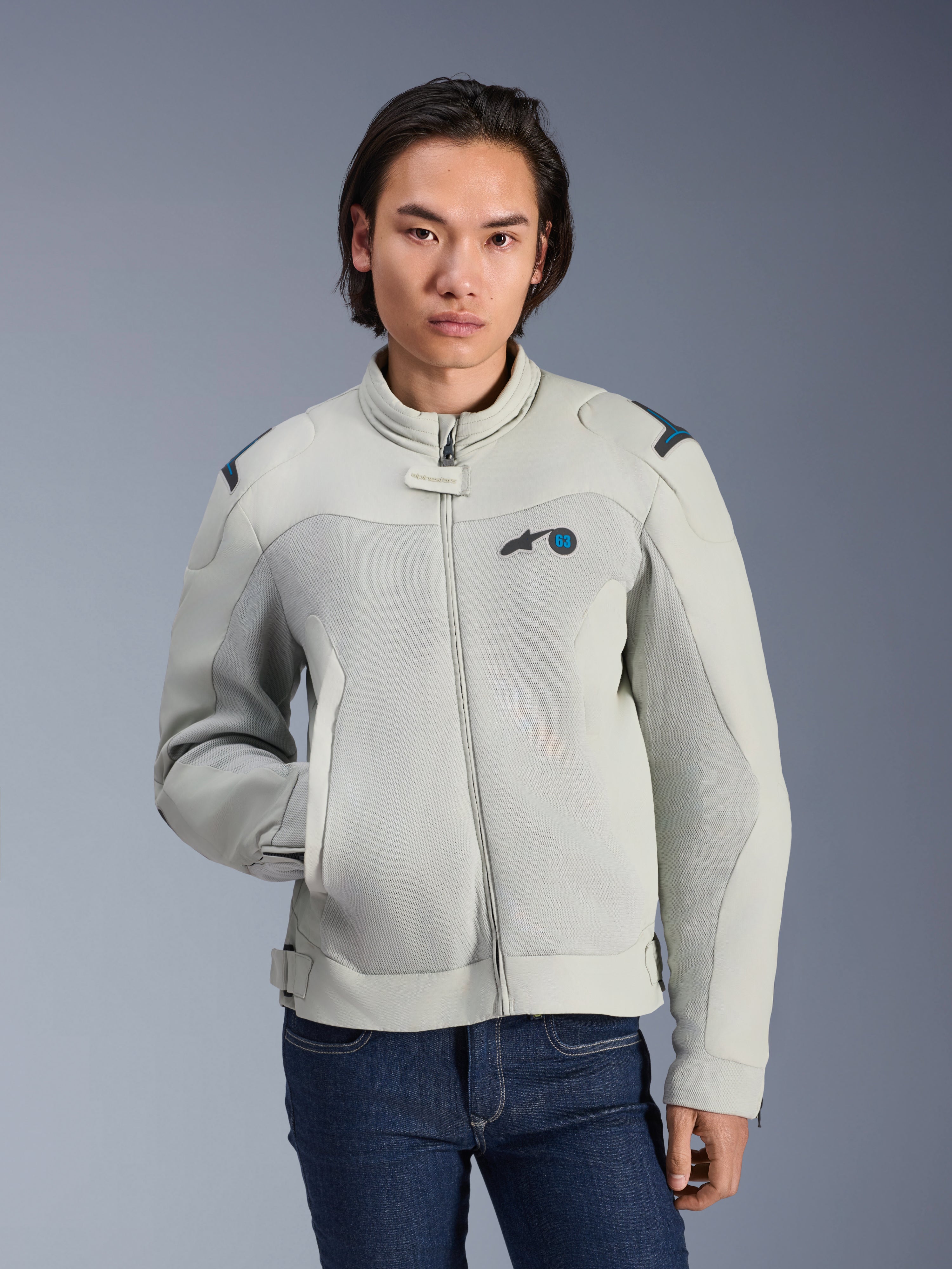 Alpinestars Circal-1 Air Jacket, kolory Metal Gray i Methyl Blue, miejska kurtka motocyklowa z siatkowymi panelami wentylacyjnymi, zapięcie na zamek i wyściełany kołnierz, noszona przez modela w niebieskich dżinsach, futurystyczny i zrównoważony design na letnią jazdę