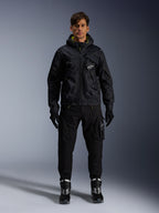 Męski model w kurtce Alpinestars Mogress Air, czarna tekstylna kurtka z kapturem i limonkowymi akcentami, zestawiona z czarnymi spodniami typu utility, czarnymi rękawicami oraz czarno-białymi butami motocyklowymi, miejski design streetwearowy inspirowany motorsportem