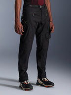 Alpinestars Acteon Pants, czarne spodnie motocyklowe prezentowane na modelu, o nowoczesnym, zwężanym kroju, z kieszeniami cargo zapinanymi na zamek, regulowanym paskiem w talii i technicznymi sneakersami, miejska odzież motocyklowa