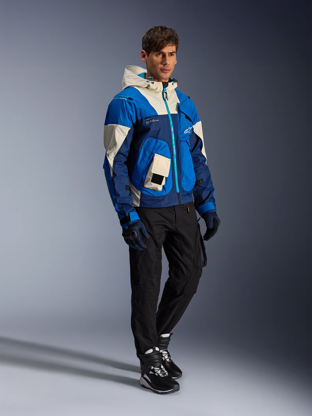 Alpinestars Mogress Air Jacket, miejska kurtka motocyklowa, kolor Blue Almond z kremowymi i granatowymi panelami, wyposażona w kaptur i kieszenie użytkowe, zestawiona z czarnymi spodniami motocyklowymi, rękawicami i butami, nowoczesna odzież ochronna inspirowana stylem streetwear.