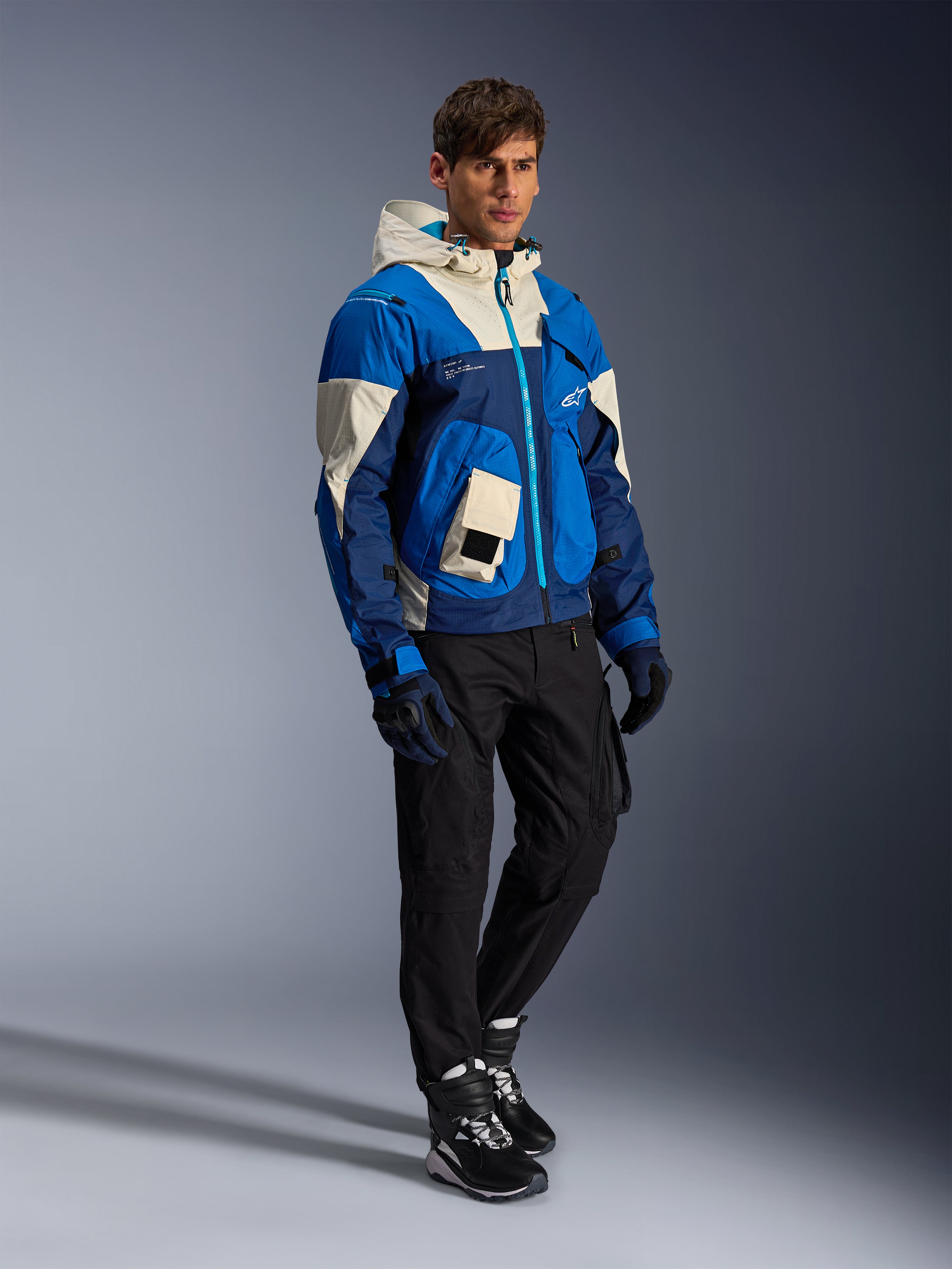 Alpinestars Mogress Air Jacket, miejska kurtka motocyklowa, kolor Blue Almond z kremowymi i granatowymi panelami, wyposażona w kaptur i kieszenie użytkowe, zestawiona z czarnymi spodniami motocyklowymi, rękawicami i butami, nowoczesna odzież ochronna inspirowana stylem streetwear.