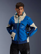 Męski model w kurtce Alpinestars Mogress Air w kolorze Blue Almond, miejska kurtka motocyklowa z jaskrawoniebieskimi i granatowymi panelami kolorystycznymi, kremowe akcenty na kapturze i kieszeniach, techniczna tkanina ripstop z kieszeniami typu utility, nowoczesny streetwear inspirowany motorsportem