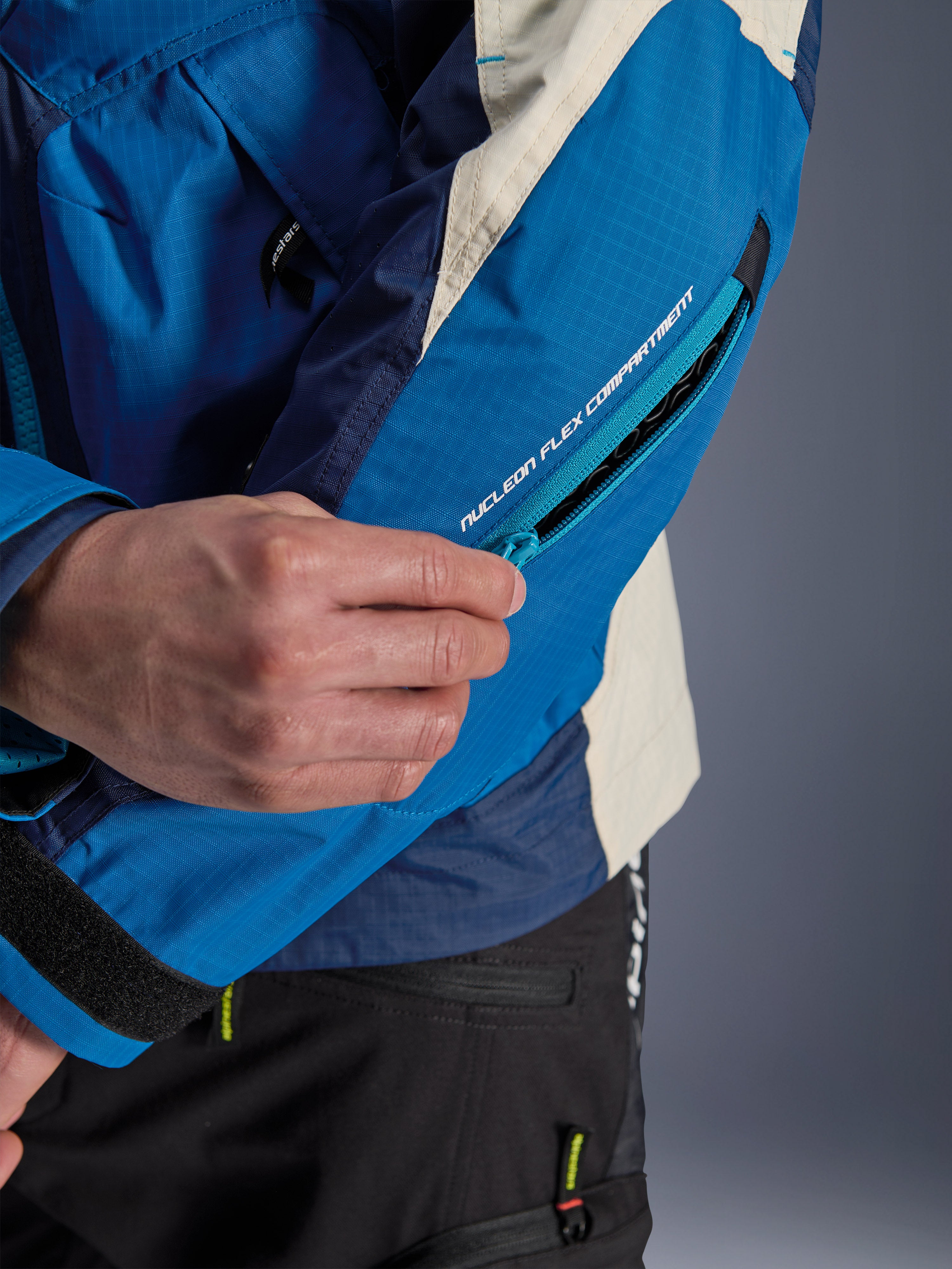 Alpinestars Mogress Air Jacket w kolorze Blue Almond, zbliżenie na rękaw z zapinaną na zamek komorą na ochraniacz Nucleon Flex, techniczna niebieska i beżowa tkanina o strukturze ripstop, detal miejskiej odzieży motocyklowej