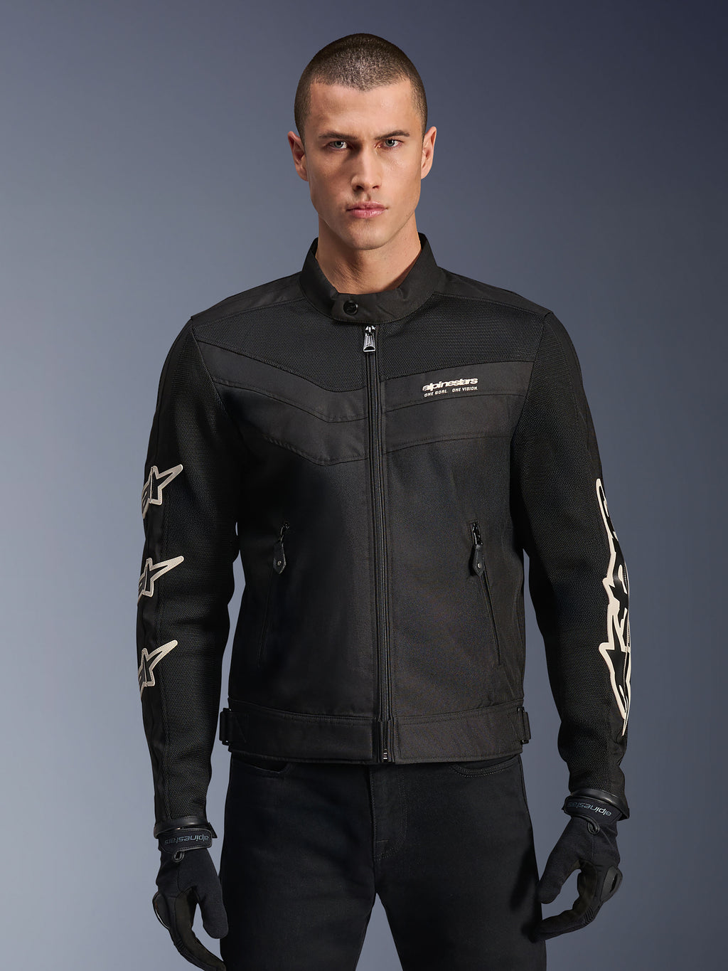 Alpinestars T-Dyno Air Jacket, czarna tekstylna kurtka motocyklowa, z białymi grafikami gwiazd na rękawach i logo na klatce piersiowej, panele z siatki zapewniające wentylację, krój motocyklowy inspirowany stylem vintage, noszona z czarnymi rękawicami i spodniami