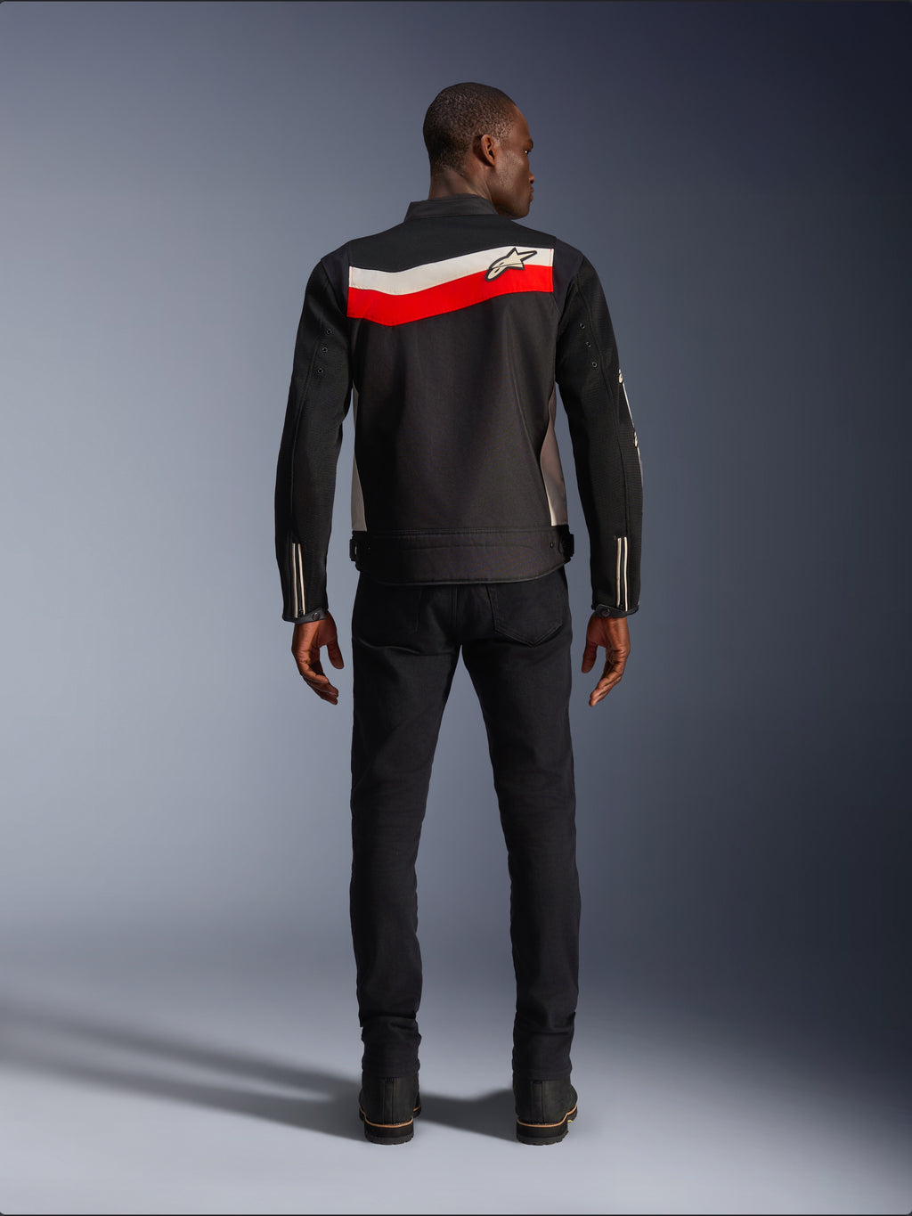 Alpinestars T-Dyno Air Jacket, męska tekstylna kurtka motocyklowa, widok z tyłu, czarna z jasnoczerwonymi i poziomymi pasami ecru na plecach, logo Alpinestars na karczku, noszona z czarnymi spodniami i butami, oddychająca konstrukcja z siatki 3D