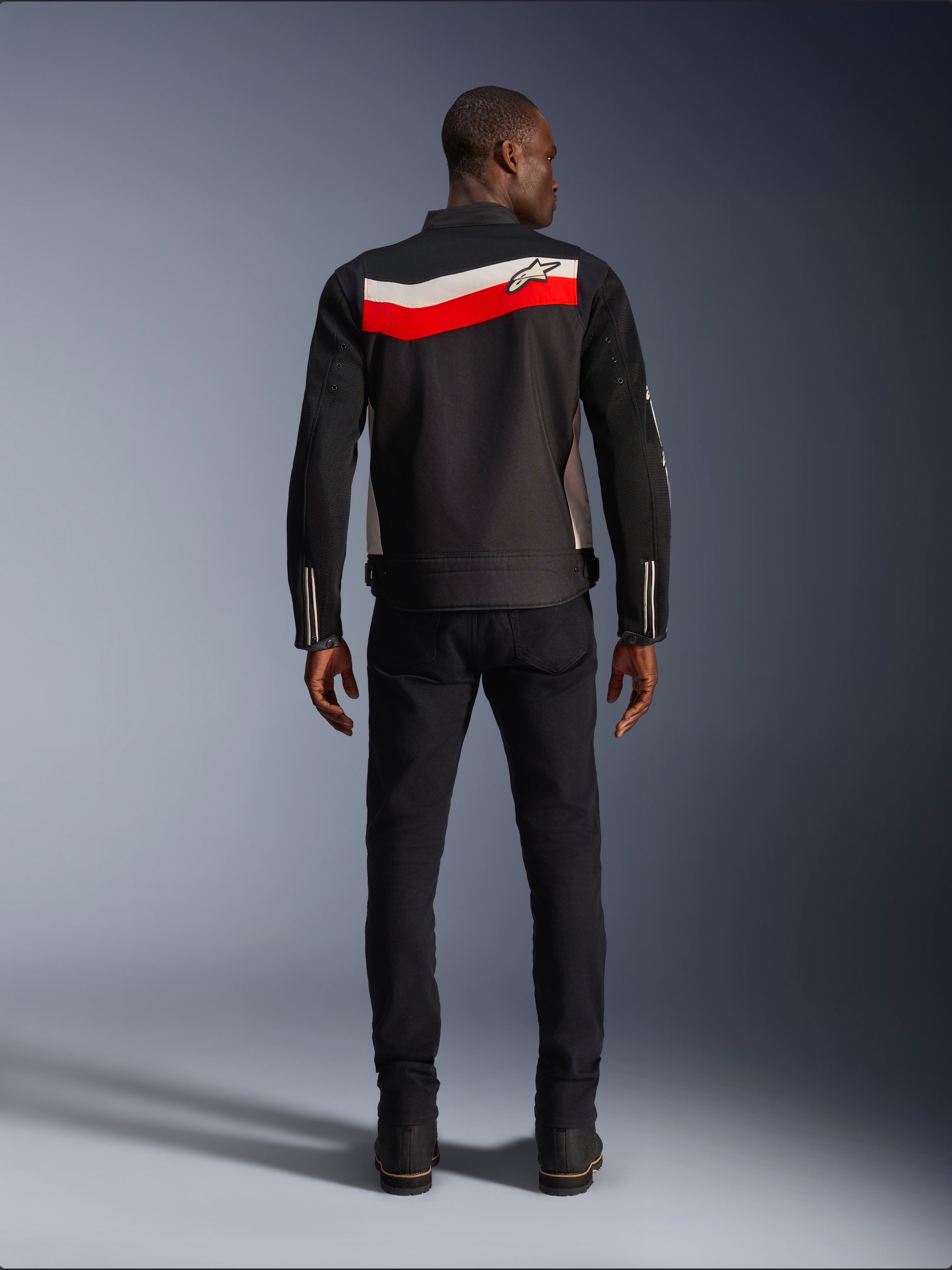 Alpinestars T-Dyno Air Jacket, męska tekstylna kurtka motocyklowa, widok z tyłu, czarna z jasnoczerwonymi i poziomymi pasami ecru na plecach, logo Alpinestars na karczku, noszona z czarnymi spodniami i butami, oddychająca konstrukcja z siatki 3D