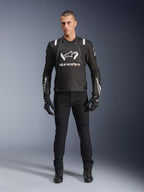 Kurtka Alpinestars T-Stunt Air, czarno-biała kurtka motocyklowa, noszona z czarnymi spodniami motocyklowymi, rękawicami i butami, z wyraźnym białym logo Alpinestars na klatce piersiowej i rękawach, sportowy krój tekstylny z panelami z siatki dla wentylacji
