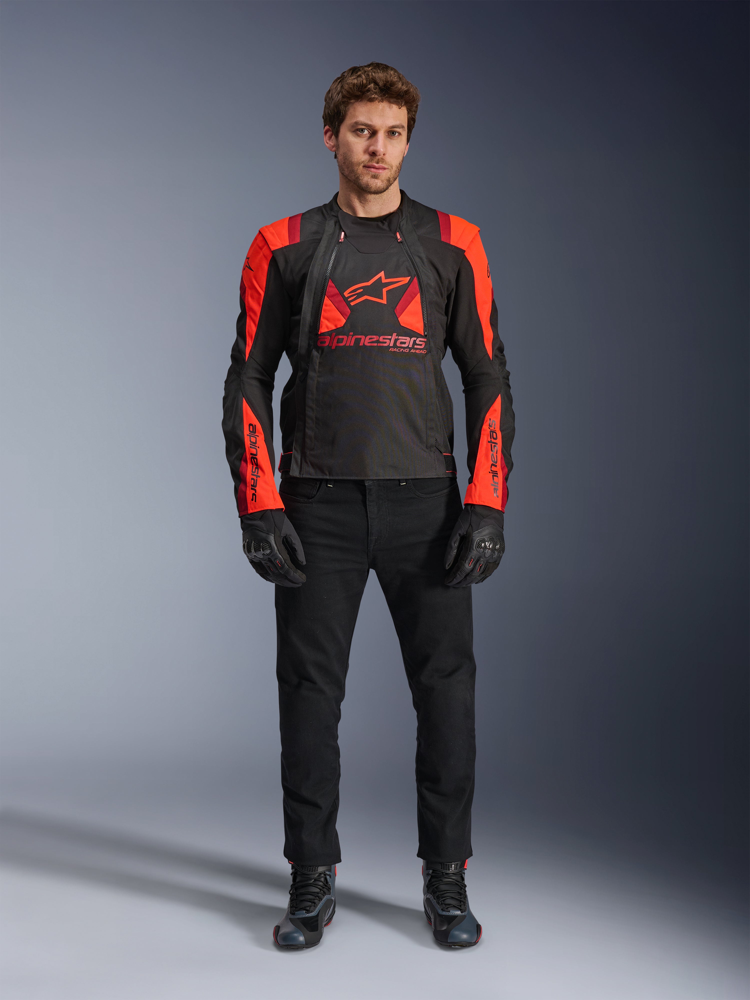 Kurtka Alpinestars T-Stunt Air, kolor czarny, neonowy czerwony i ciemnoczerwony, noszona przez modela z czarnymi jeansami i rękawicami, modułowa konstrukcja 2-w-1 z dużymi panelami z siatki zapewniającymi przepływ powietrza, sportowy krój do jazdy szosowej