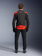 Kurtka Alpinestars T-Stunt Air, czarna z akcentami Red Fluo i ciemnoczerwonymi, widok z tyłu na modelu, w zestawieniu z czarnymi spodniami i butami motocyklowymi, wyraźne logo Alpinestars na dolnym panelu pleców, modułowa konstrukcja z siateczki zapewniająca wentylację