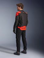 Mężczyzna w kurtce Alpinestars T-Stunt Air Jacket, widok z tyłu, kolor czarny, neonowy czerwony i ciemnoczerwony, tekstylna kurtka motocyklowa z panelami z siatki o sportowym kroju, z wyraźnym brandingiem Alpinestars na dole pleców, zestawiona z czarnymi spodniami i butami motocyklowymi