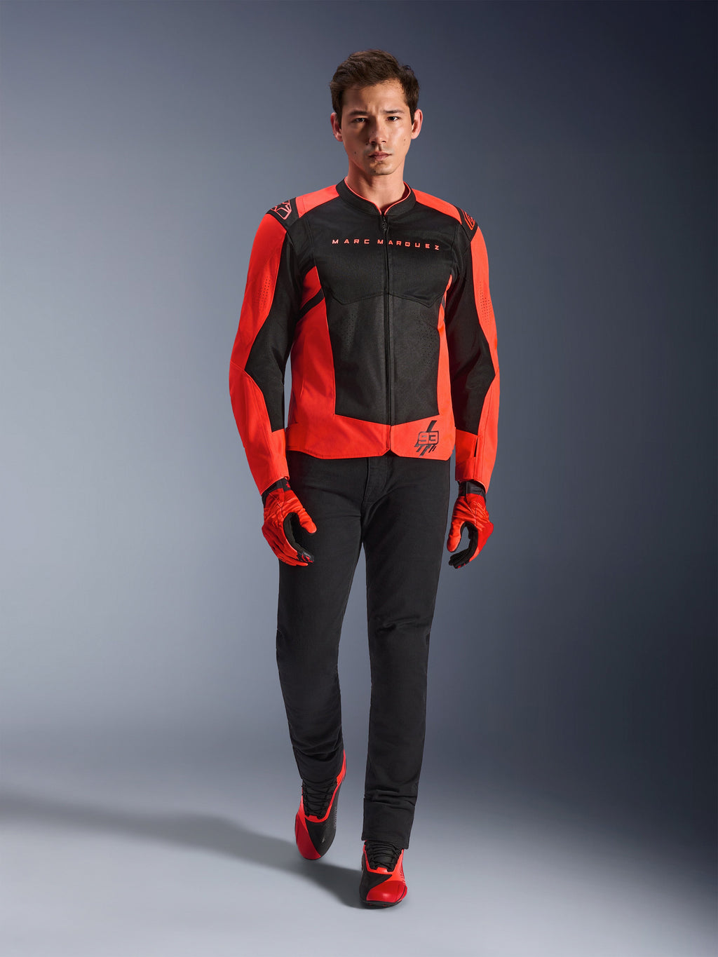Alpinestars MM93 T-SPS Air V2 Jacket, czerwono-czarna (Red Fluo Black), noszona przez modela z dopasowanymi czerwonymi rękawicami i czarnymi spodniami, z brandingiem Marca Marqueza i logo 93, wentylowana sportowa kurtka motocyklowa do jazdy miejskiej