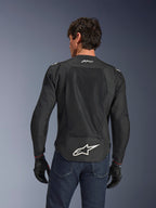 Alpinestars FQ20 T-SPS Air V2 Monster Jacket, Black, Rear view featuring large ventilation mesh panels and white Alpinestars logo on the lower back, worn with blue jeans and black motorcycle gloves, urban sport riding style.