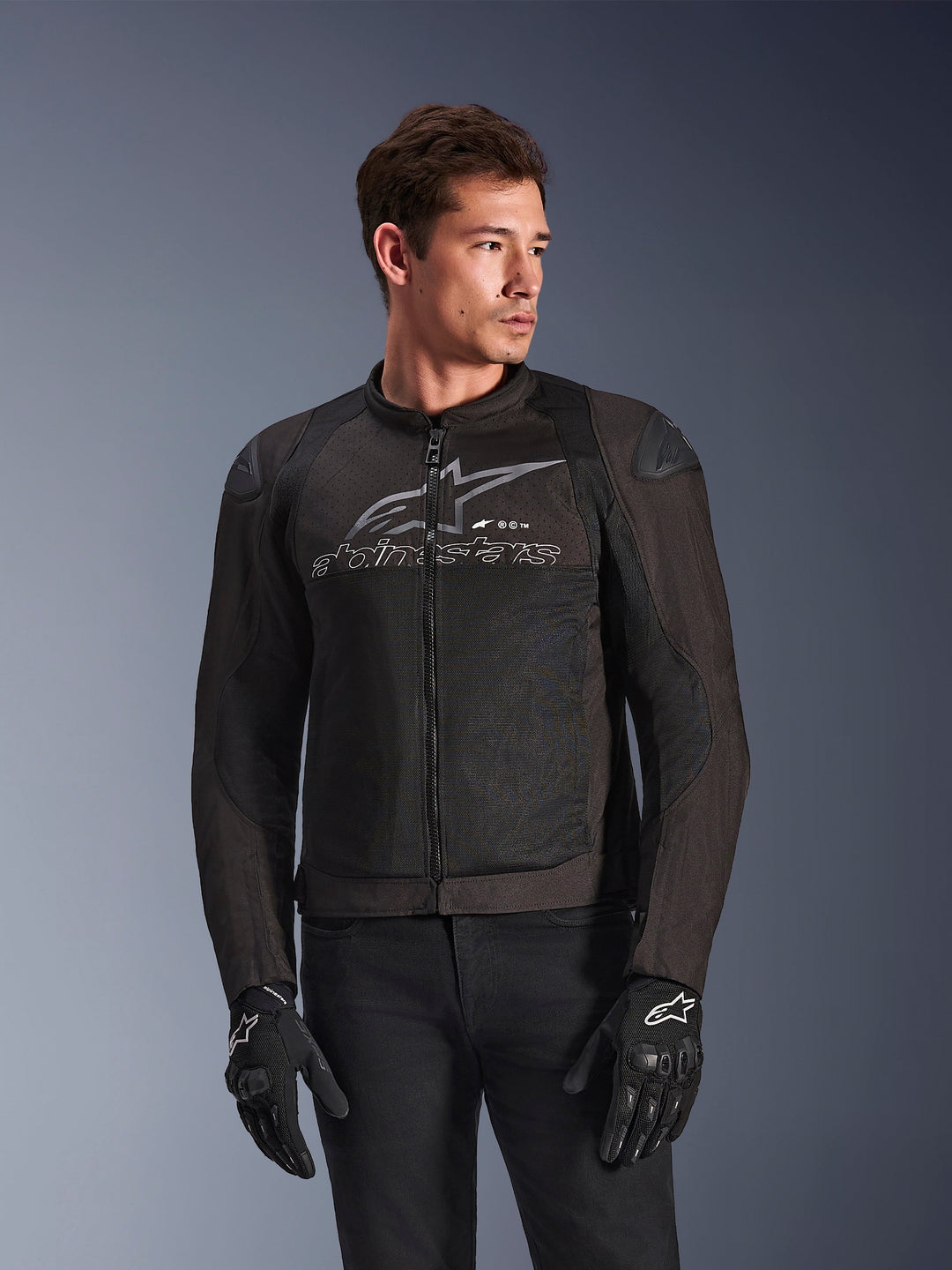 Kurtka Alpinestars SMX Air w kolorze Black Anthracite, tekstylna kurtka motocyklowa z panelami z siatki o wysokim przepływie powietrza, duże szare logo i napis Alpinestars na klatce piersiowej, slidery ramion DFS Lite, model w czarnych rękawicach motocyklowych, sportowy styl jazdy
