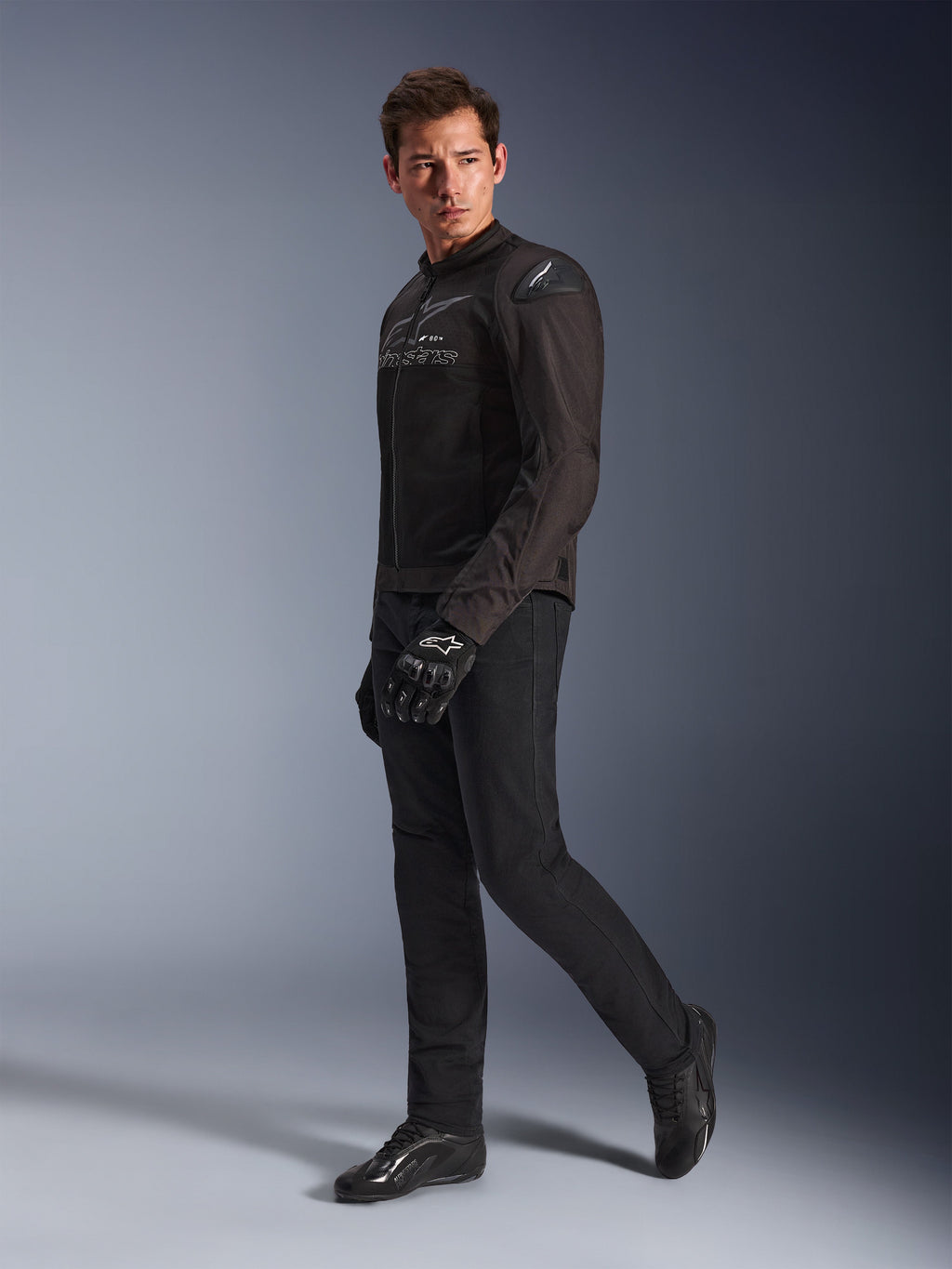 Kurtka Alpinestars SMX Air w kolorze Black Anthracite, model ubrany w pasujące czarne spodnie motocyklowe, rękawice i buty, studyjne ujęcie całej sylwetki, sportowa odzież motocyklowa z siatki technicznej i sliderami na ramionach