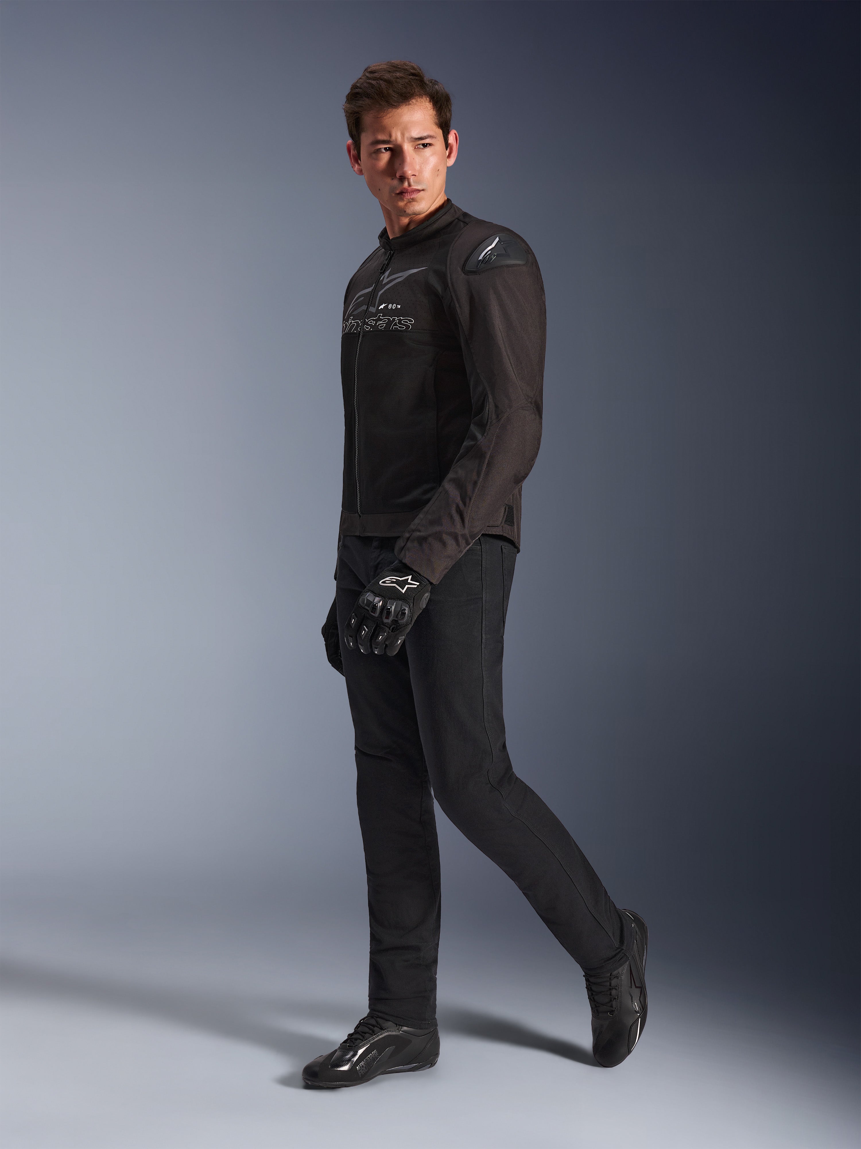 Kurtka Alpinestars SMX Air w kolorze Black Anthracite, model ubrany w pasujące czarne spodnie motocyklowe, rękawice i buty, studyjne ujęcie całej sylwetki, sportowa odzież motocyklowa z siatki technicznej i sliderami na ramionach