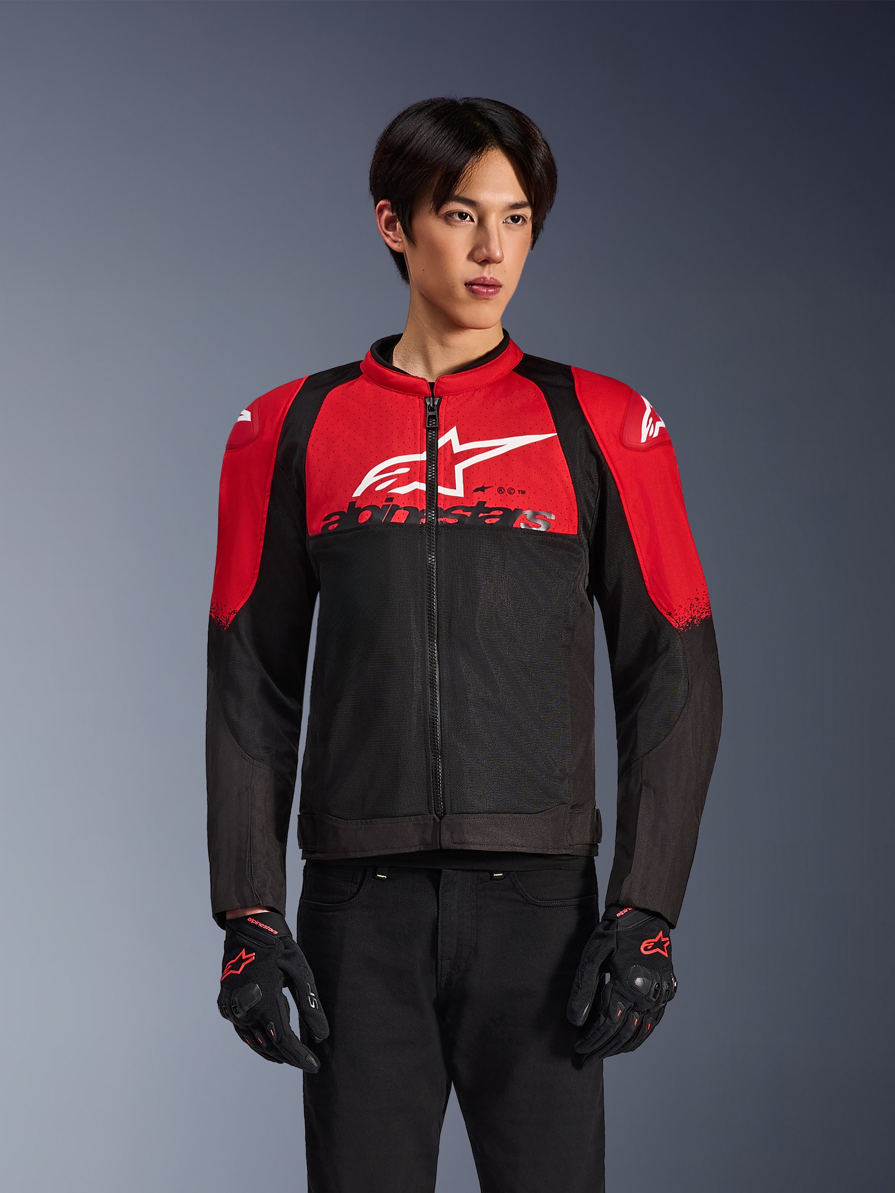 Alpinestars SMX Air Jacket, motocyklowa kurtka siatkowa, jaskrawoczerwona i czarna, noszona przez modela w czarnych rękawicach motocyklowych, z dużym białym logo na piersi, wentylowana konstrukcja tekstylna z czerwonymi panelami na ramionach i czarnymi rękawami, sportowa odzież do jazdy w ciepłe dni