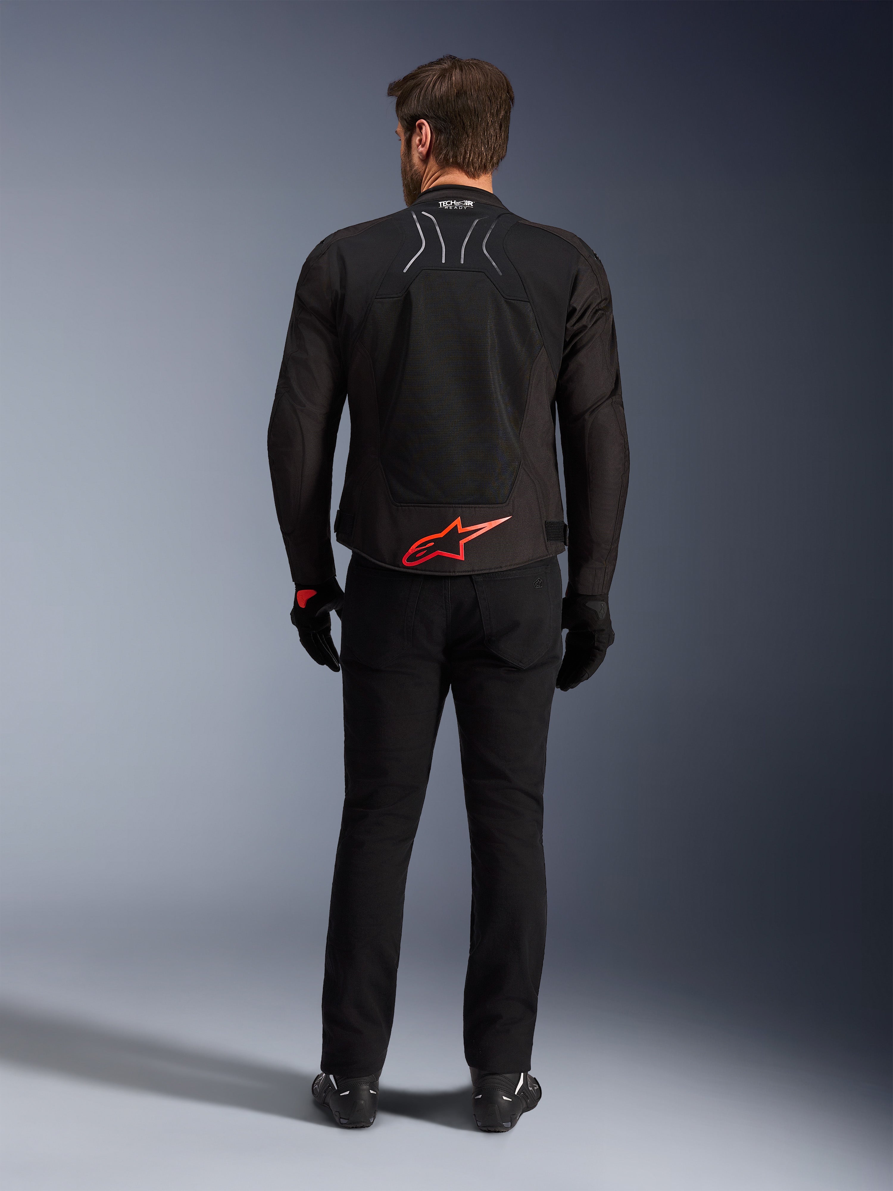 Alpinestars SMX Air Jacket, czarna z jaskrawoczerwonym logo, widok z tyłu ukazujący oznaczenie Tech-Air Ready i siatkowe panele wentylacyjne, noszona z czarnymi spodniami i rękawicami, wysokiej klasy sportowa i wyścigowa odzież motocyklowa