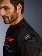 Alpinestars SMX Air Jacket, czarno-czerwona, zbliżenie na ochraniacz ramion DFS Lite z logo gwiazdy, noszona przez mężczyznę z brodą, tekstylna sportowa i wyścigowa kurtka motocyklowa.