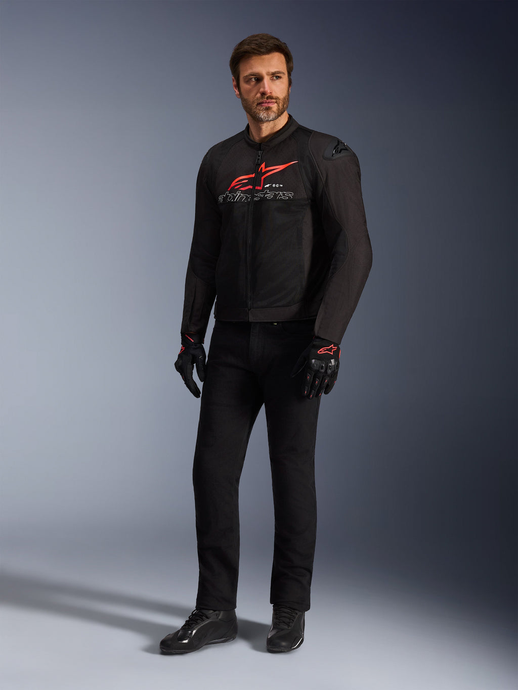 Męski model w kurtce Alpinestars SMX Air Jacket w kolorze Black Bright Red White, czarne spodnie techniczne, czarno-czerwone rękawice i czarne buty motocyklowe, z wyraźnym czerwonym logo na klatce piersiowej i białym brandingiem, studyjne ujęcie całej sylwetki, sportowa odzież motocyklowa.