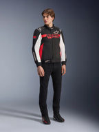 Alpinestars Monza Sport Jacket, czarno-czerwono-biała tekstylna kurtka motocyklowa, design inspirowany wyścigami z brandingiem ASTARS na klatce piersiowej i rękawach, noszona przez modela z czarnymi spodniami i butami motocyklowymi, casualowa odzież motocyklowa w sportowym stylu