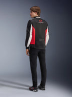 Kurtka Alpinestars Monza Sport, tekstylna kurtka motocyklowa, czarna z jaskrawoczerwonymi i białymi elementami, widok modelu od tyłu z czerwonymi panelami bocznymi i białymi akcentami na rękawach, logo Alpinestars i napis „ONE GOAL. ONE VISION.”, zestawiona z czarnymi spodniami i butami motocyklowymi w sportowym stylu