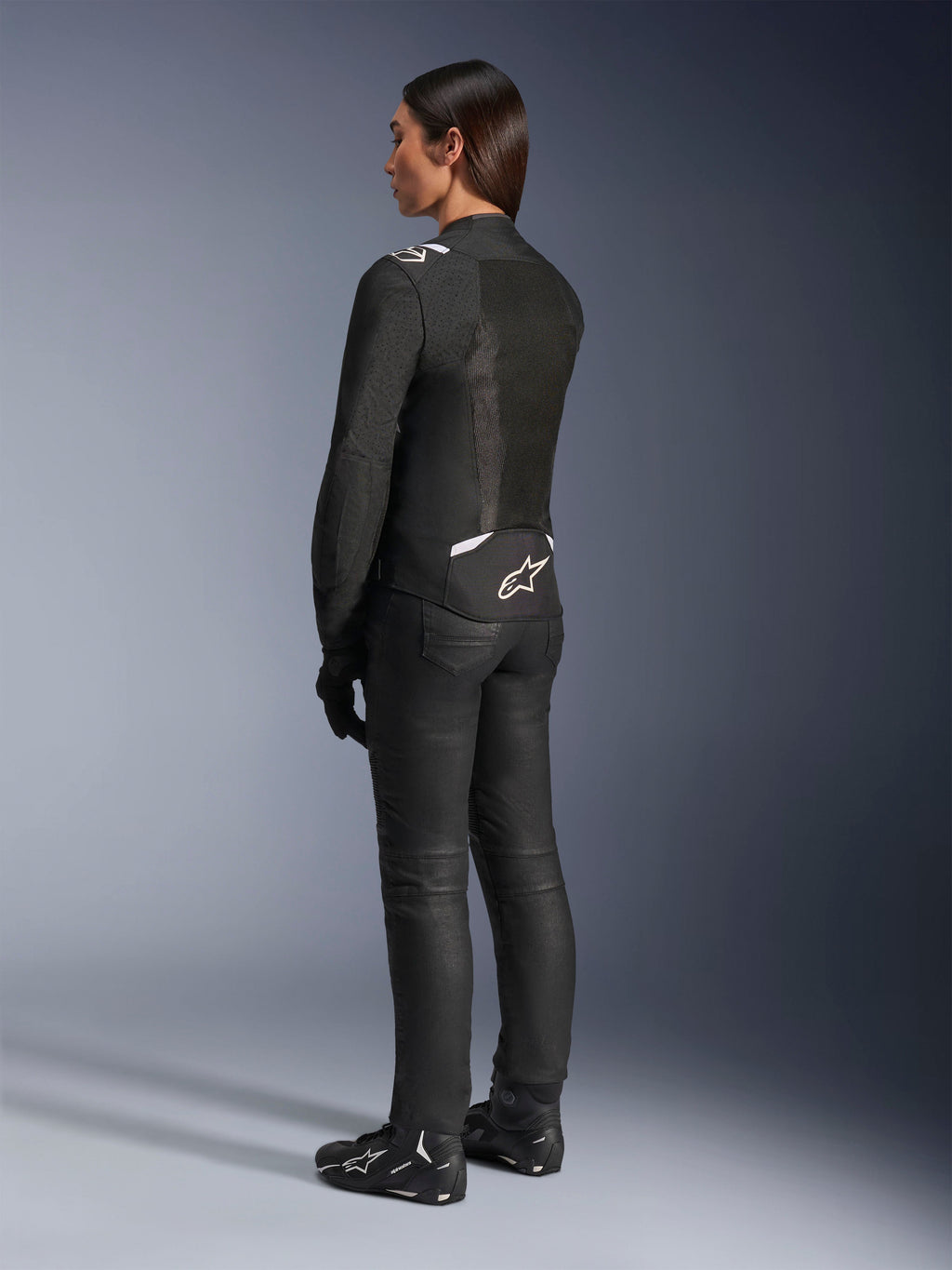 Kurtka Alpinestars Stella T-Sps Air V2, czarno-biała, widok z tyłu ukazujący panele z siatki i logo w dolnej części pleców, zestawiona z czarnymi spodniami i butami motocyklowymi, sportowa tekstylna odzież szosowa dla kobiet