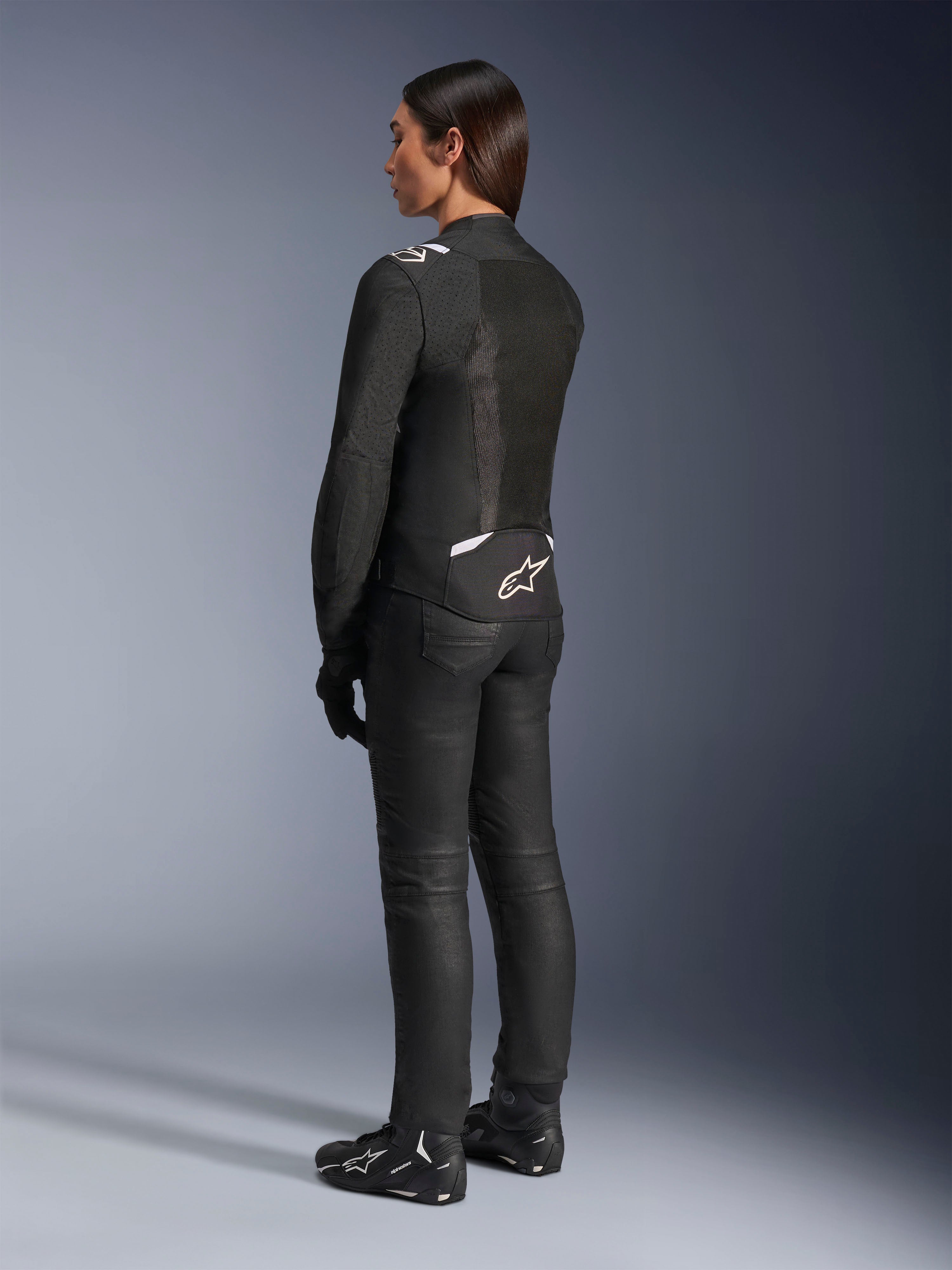 Kurtka Alpinestars Stella T-Sps Air V2, czarno-biała, widok z tyłu ukazujący panele z siatki i logo w dolnej części pleców, zestawiona z czarnymi spodniami i butami motocyklowymi, sportowa tekstylna odzież szosowa dla kobiet