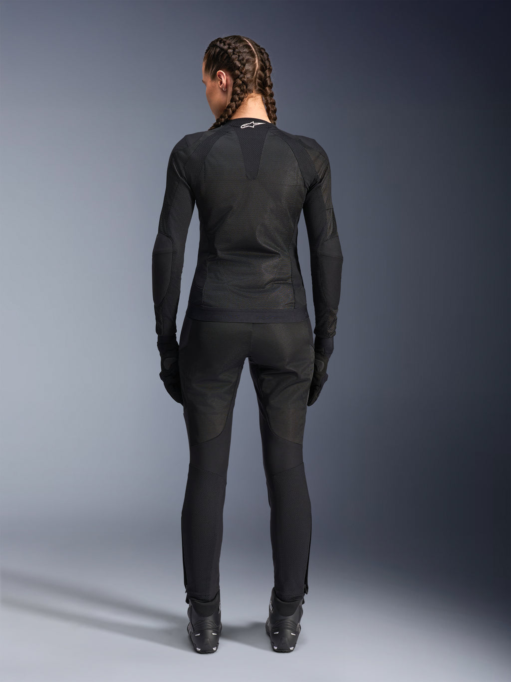 Alpinestars Stella Troop-Air Jacket, damska kurtka motocyklowa, czarna, widok z tyłu motocyklistki ubranej w techniczną kurtkę z siatki, zestawioną z pasującymi czarnymi spodniami motocyklowymi, rękawicami i butami, dopasowany, oddychający design z białym logo Alpinestars na kołnierzu