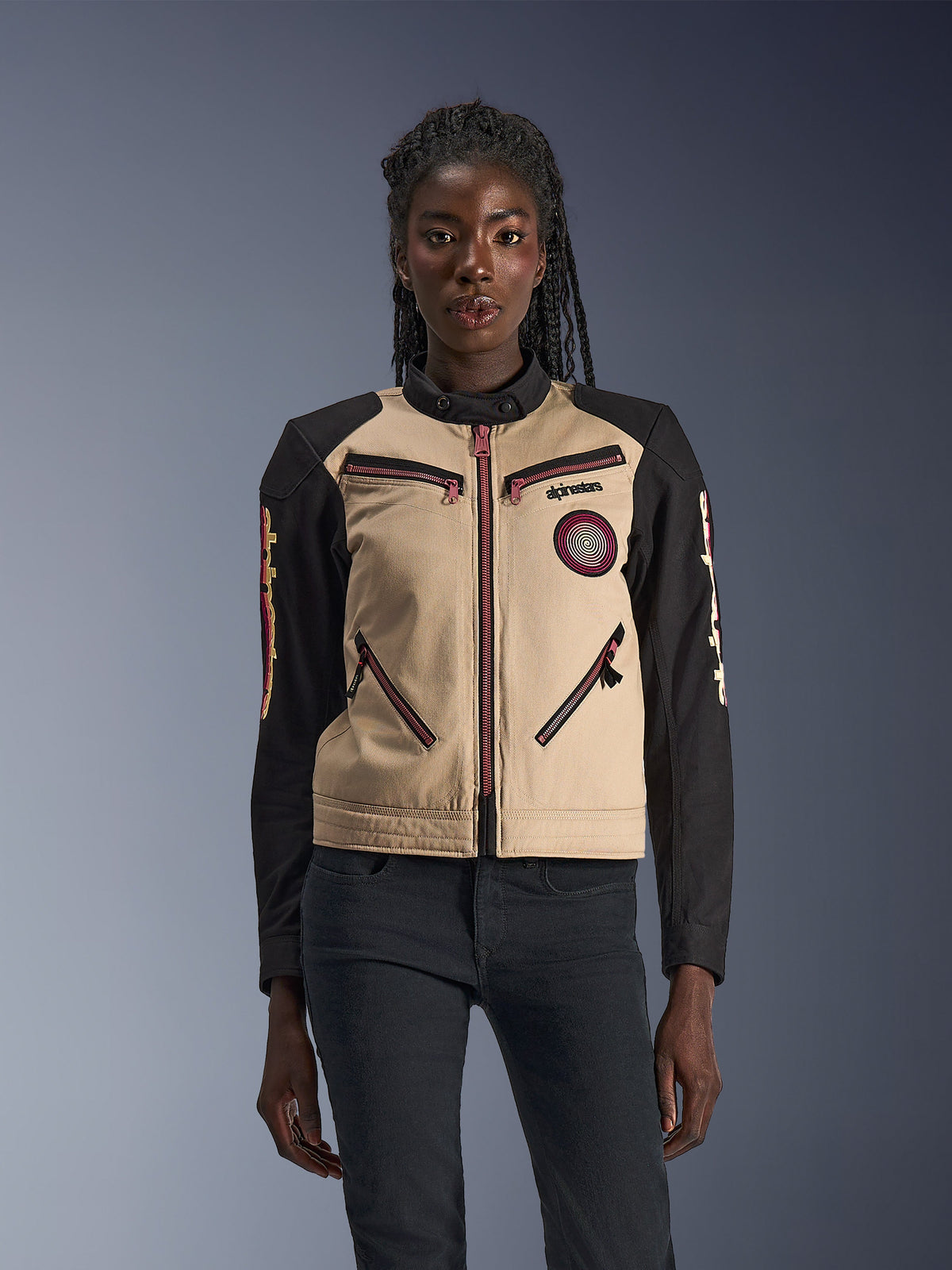 Alpinestars Stella Grace Jacket, damska kurtka motocyklowa, kolor aluminium i czarny, design inspirowany odzieżą roboczą z różowo-czerwonymi akcentami na zamkach, spiralna naszywka na piersi, długie czarne rękawy z żółtą i czerwoną grafiką, prezentowana przez modelkę