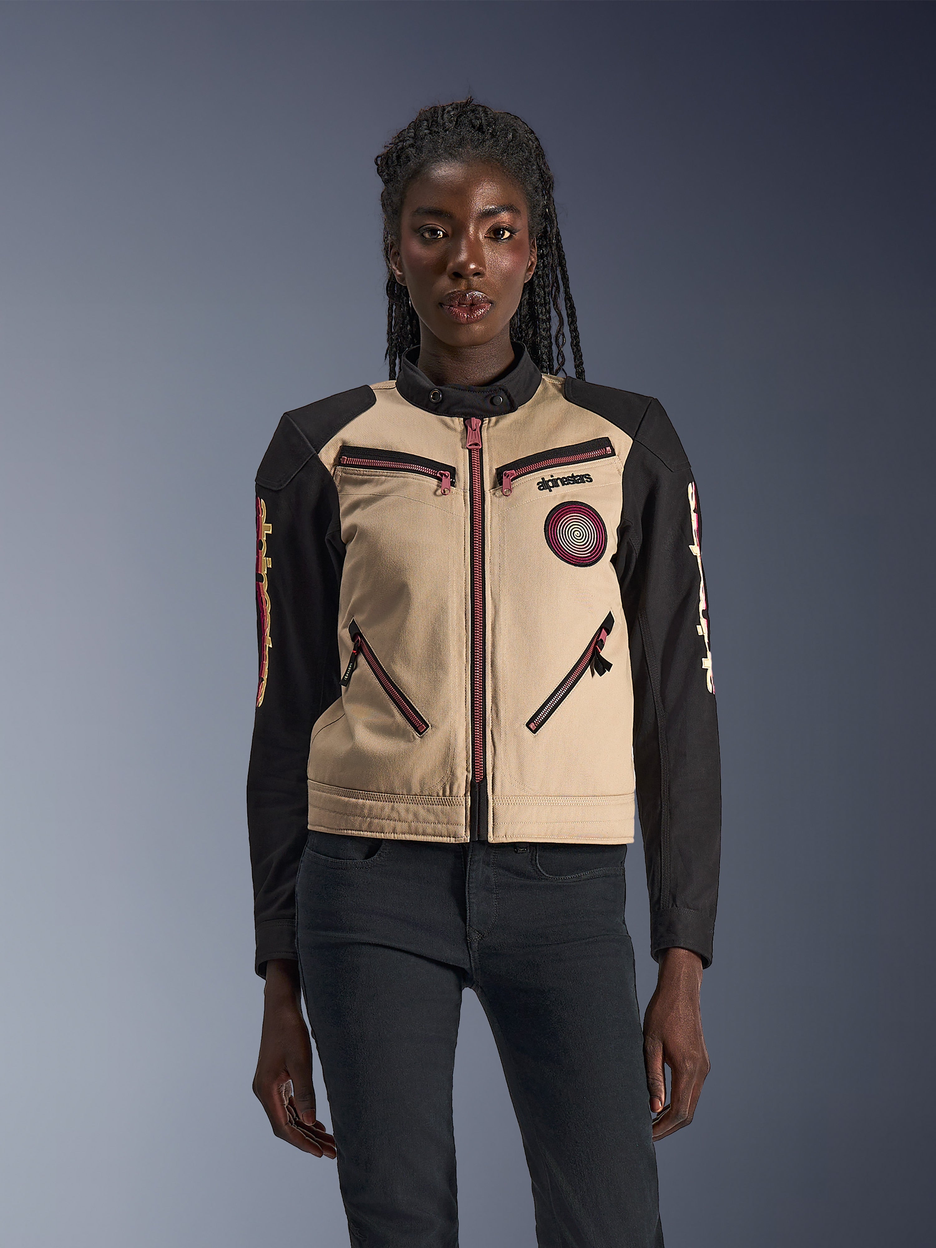 Alpinestars Stella Grace Jacket, damska kurtka motocyklowa, kolor aluminium i czarny, design inspirowany odzieżą roboczą z różowo-czerwonymi akcentami na zamkach, spiralna naszywka na piersi, długie czarne rękawy z żółtą i czerwoną grafiką, prezentowana przez modelkę