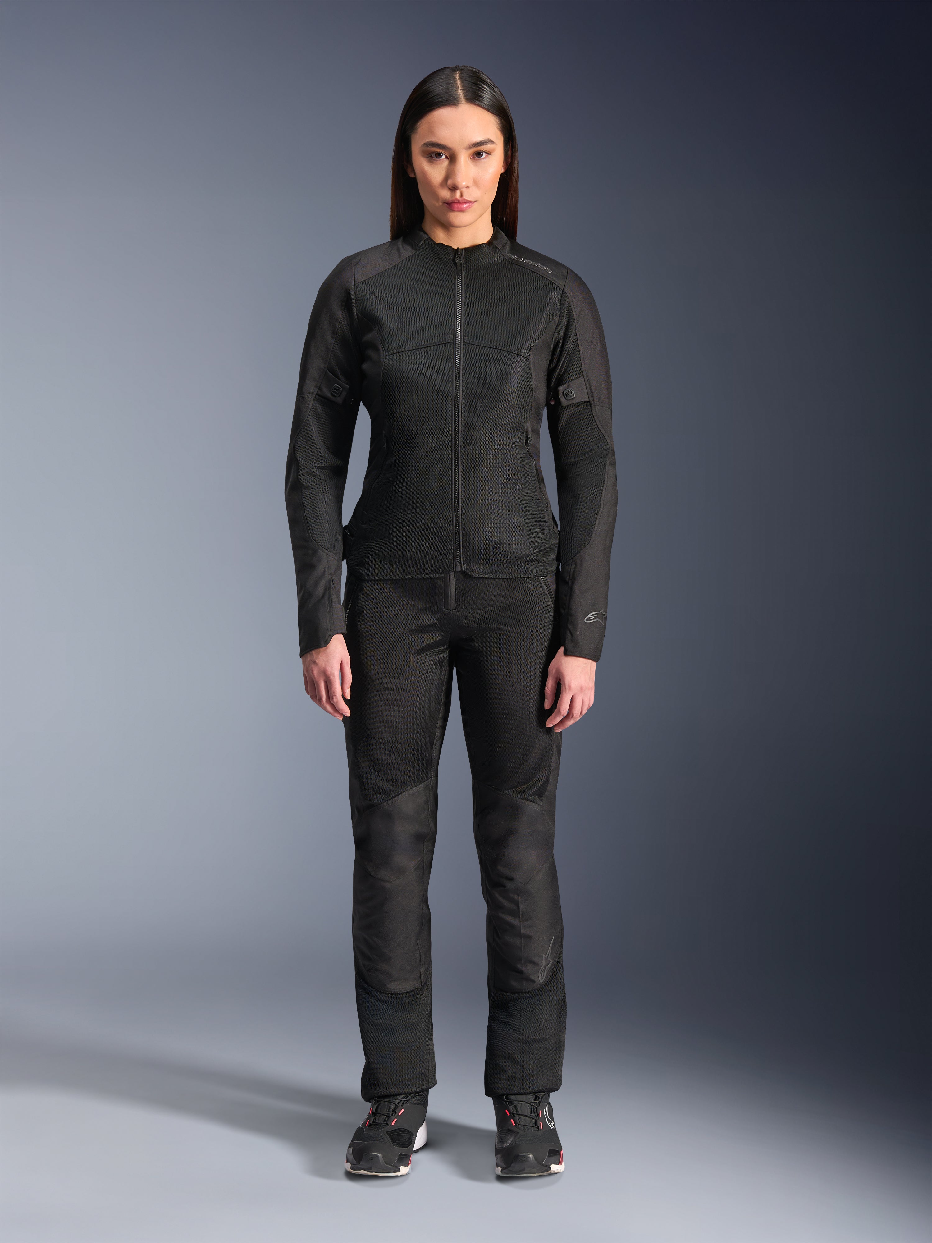Kobieta ubrana w kurtkę Alpinestars Stella C-1 Air w kolorze czarnym, zestawioną z dopasowanymi czarnymi spodniami tekstylnymi i butami motocyklowymi, o smukłym miejskim designie z dużymi panelami z siatki zapewniającymi przepływ powietrza.