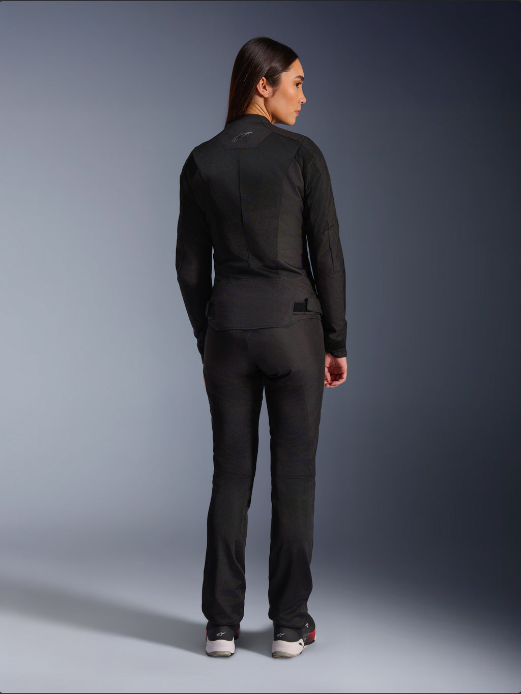 Alpinestars Stella C-1 Air Jacket, damska tekstylna kurtka motocyklowa, czarna, widok z tyłu ukazujący konstrukcję z siatki i subtelne logo w górnej części pleców, noszona z dopasowanymi czarnymi spodniami motocyklowymi, współczesny styl miejski