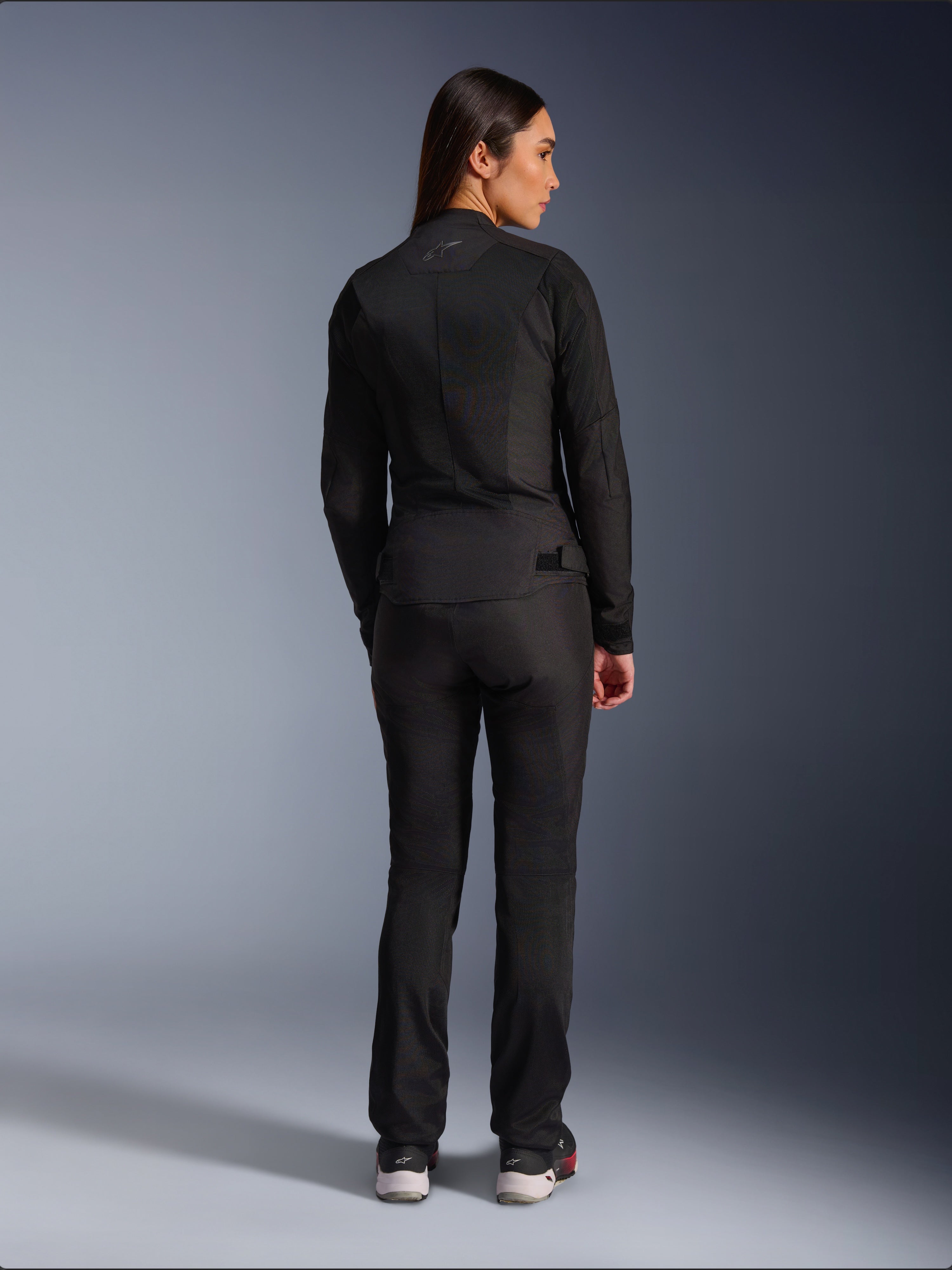 Alpinestars Stella C-1 Air Jacket, damska tekstylna kurtka motocyklowa, czarna, widok z tyłu ukazujący konstrukcję z siatki i subtelne logo w górnej części pleców, noszona z dopasowanymi czarnymi spodniami motocyklowymi, współczesny styl miejski