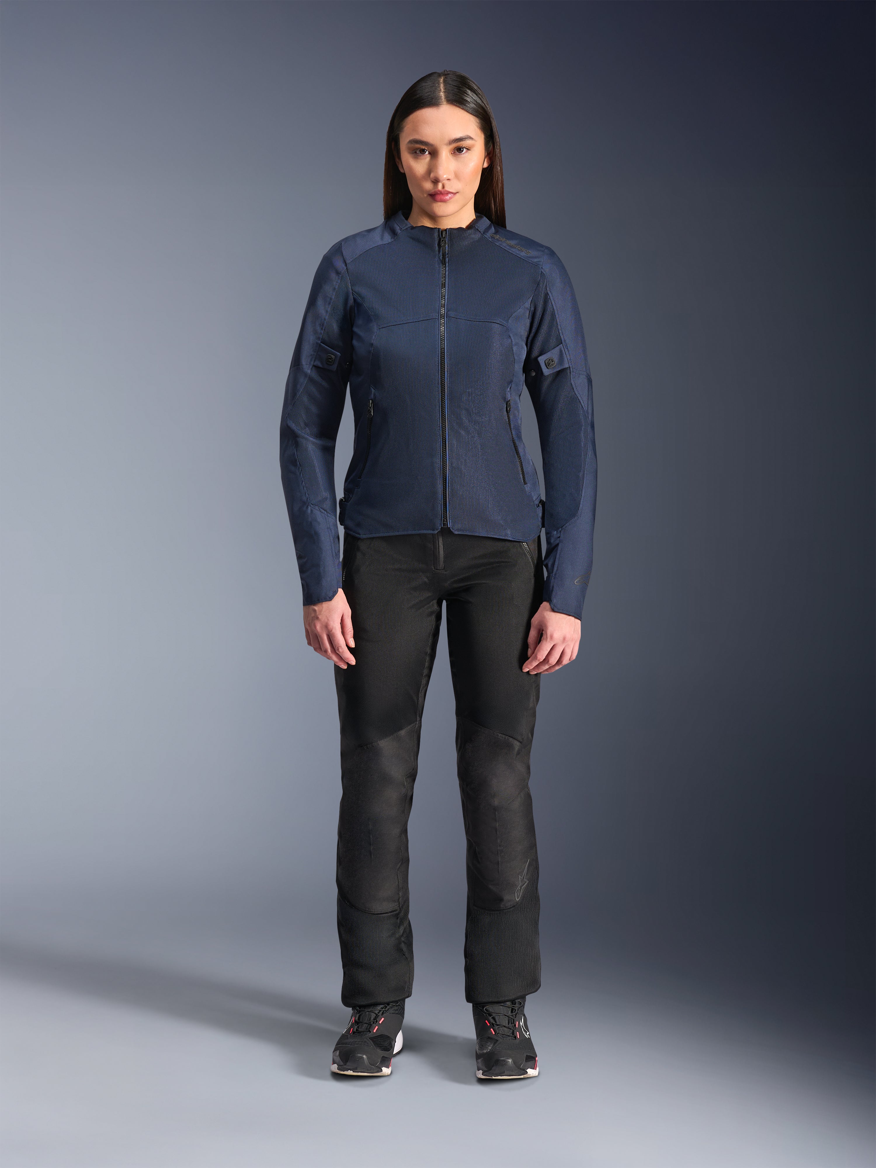Modelka ubrana w kurtkę Alpinestars Stella C-1 Air w kolorze niebieskim, miejska kurtka motocyklowa z panelami z siatki technicznej, czarne spodnie motocyklowe i czarne sneakersy, widok z przodu w studiu