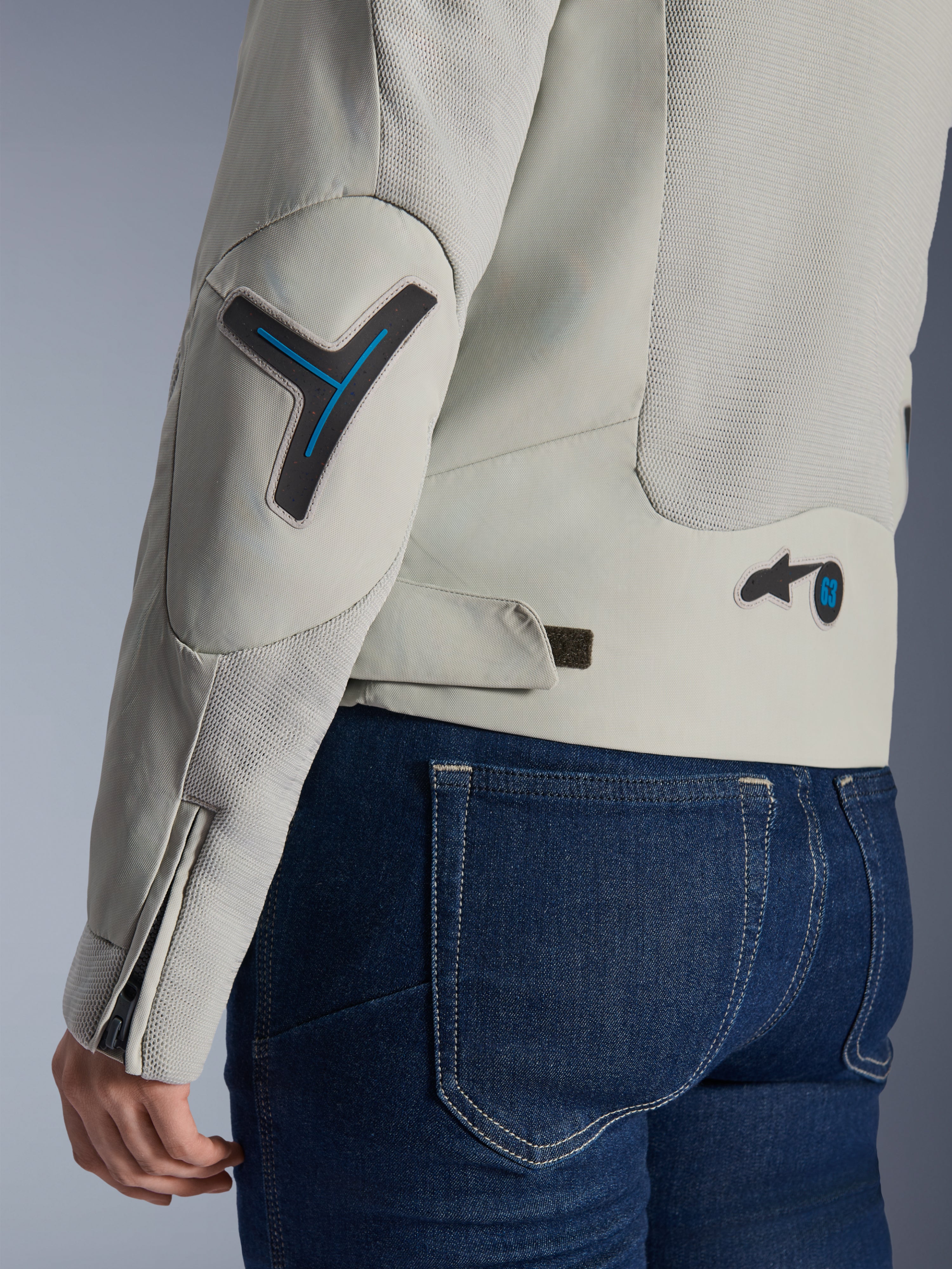 Damska kurtka Alpinestars Stella Circal-1 Air w kolorze Metal Gray i Methyl Blue, zbliżenie na tył i detal rękawa z siatkowymi panelami wentylacyjnymi, neonowo-niebieskie akcenty na łokciu i w talii, pasek do regulacji, noszona z ciemnoniebieskimi jeansami.