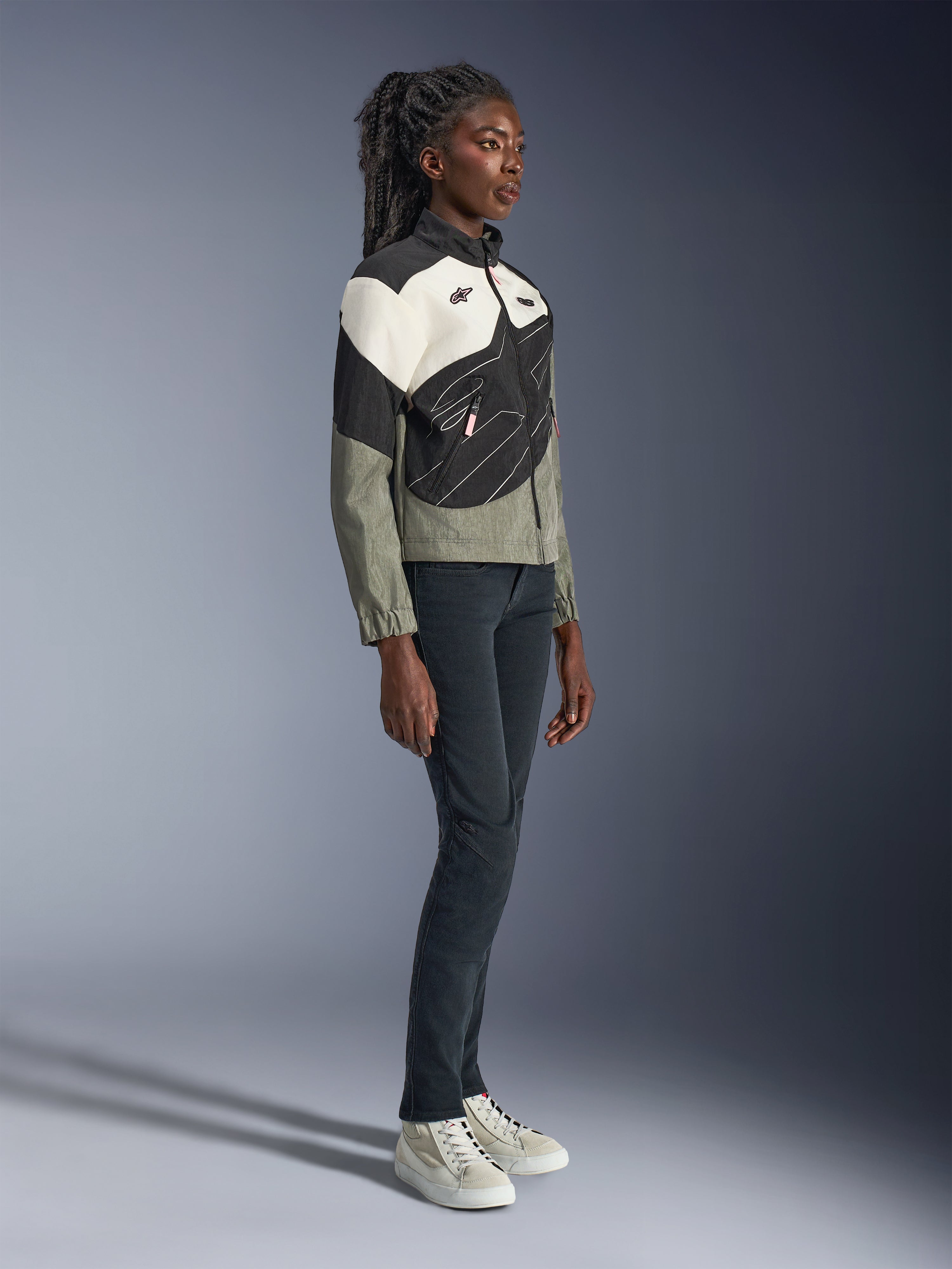 Kurtka Alpinestars Stella Moshell, damska miejska kurtka motocyklowa, szara, czarna i złamana biel z różowymi akcentami, pełna sylwetka modelki w ciemnych spodniach i trampkach, nowoczesny design inspirowany stylem streetwear do jazdy miejskiej