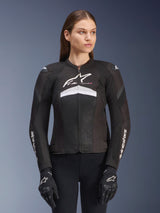 Alpinestars Stella T-GP Plus R V4 Airflow Jacket, Women's textile motorcycle jacket, Black and White, featuring extensive mesh ventilation panels on the chest, white Alpinestars logo, and a sport-fit design, worn by a model with black riding gloves and pants