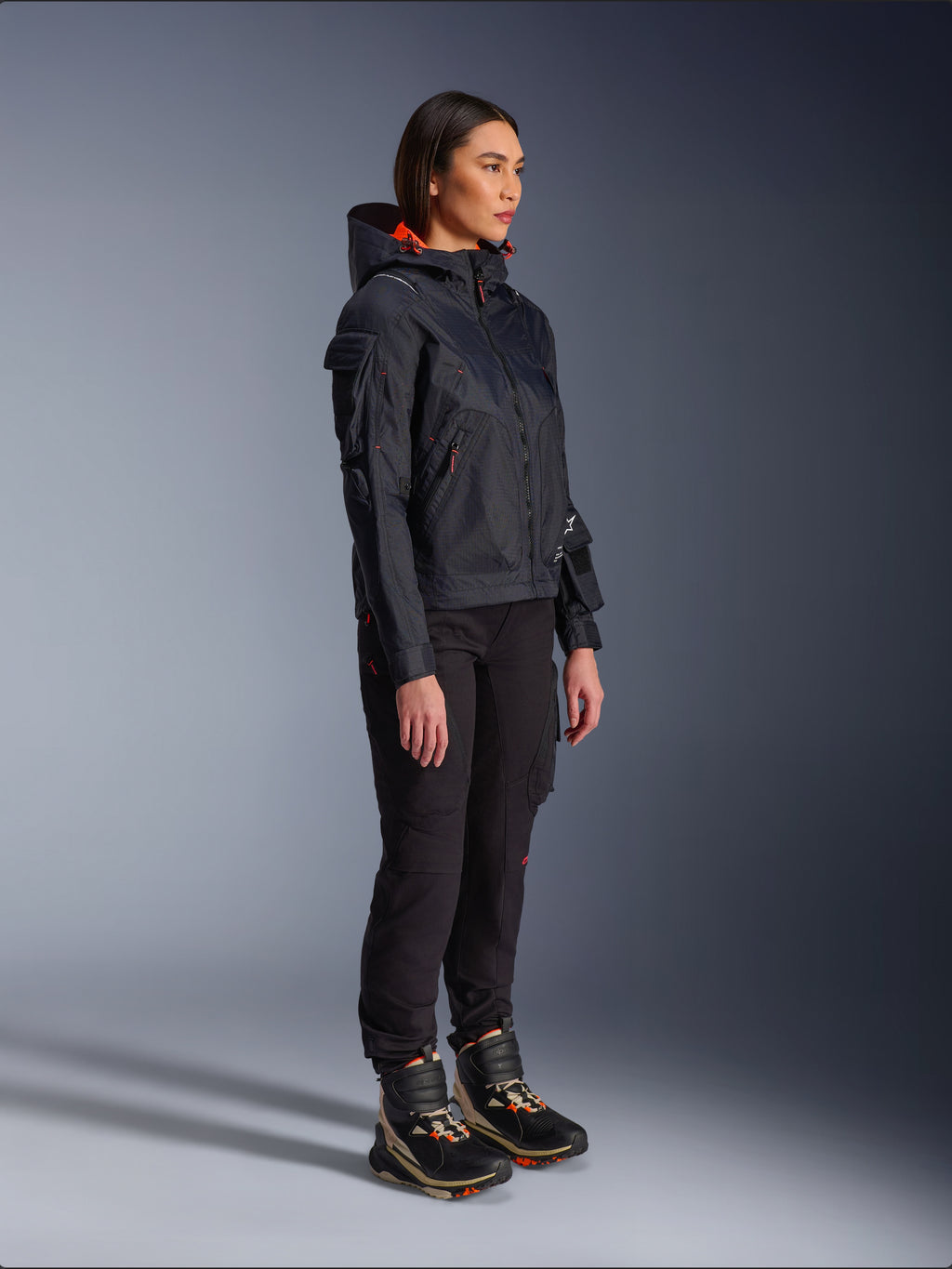 Damskie spodnie Alpinestars Actea w kolorze czarnym, krój regular fit z kieszeniami cargo, zestawione z czarną kurtką Molly Air z pomarańczowymi akcentami i wysokimi butami motocyklowymi, współczesna miejska odzież motocyklowa dla kobiet
