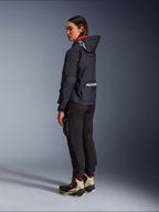 Motocyklistka w kurtce Alpinestars Molly Air Jacket w kolorze Black Fluo Coral, widok z boku i z tyłu prezentujący kaptur z logo Astars i duże logo Alpinestars na plecach, czarne spodnie motocyklowe cargo oraz beżowo-czarne buty adventure, nowoczesna miejska odzież motocyklowa dla kobiet