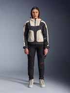 Modelka w kurtce Alpinestars Molly Air Jacket w kolorze Black Almond, design typu color-block z kremowymi i czarnymi panelami oraz kapturem z czerwoną podszewką, czarne spodnie motocyklowe i kremowe sneakersy, studyjne zdjęcie współczesnej miejskiej odzieży motocyklowej