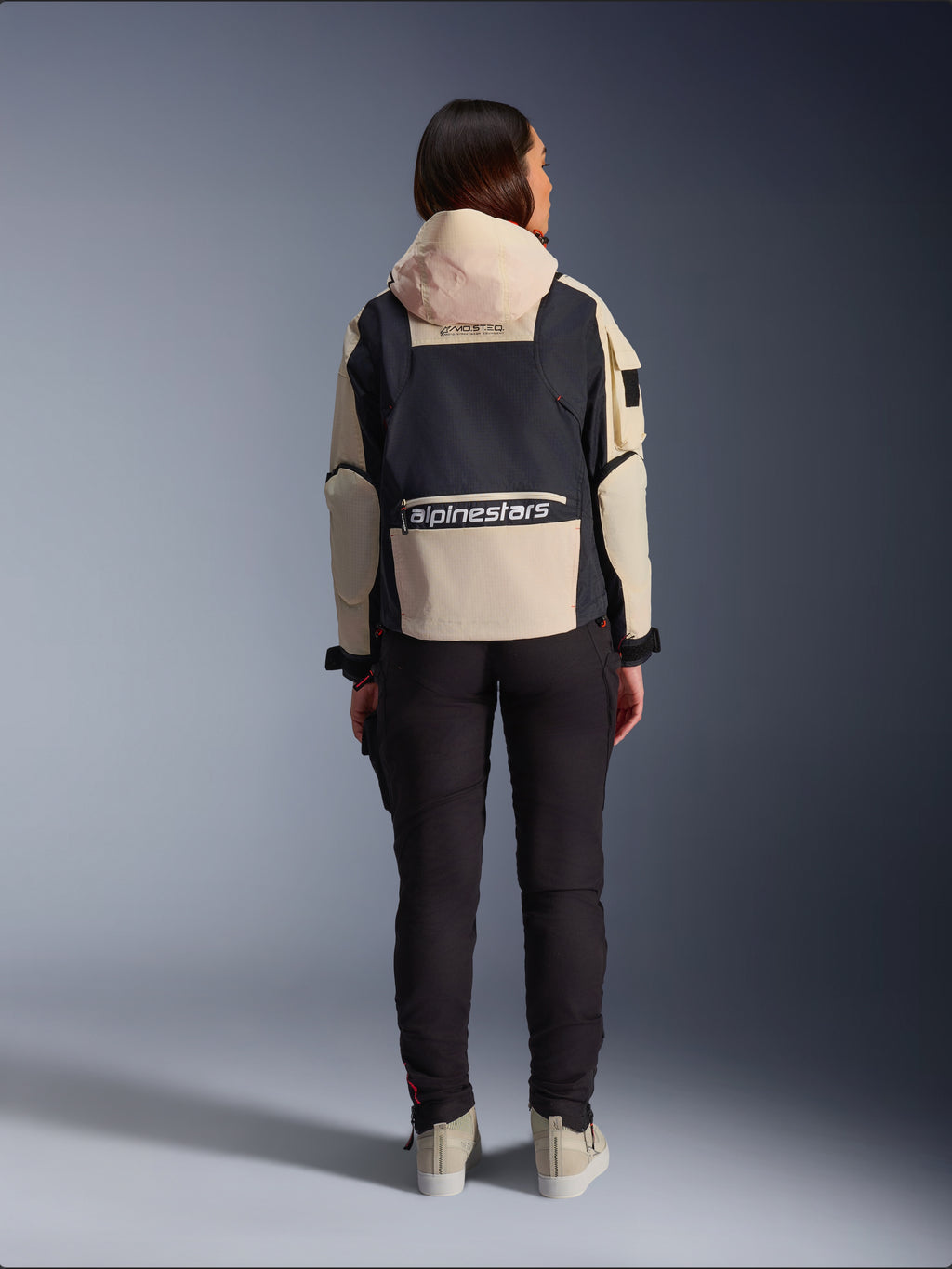 Alpinestars Molly Air Jacket, damska kurtka motocyklowa, Black Almond, widok z tyłu prezentujący kaptur i duże logo na plecach, design ripstop inspirowany stylem użytkowym, zestawiona z czarnymi spodniami motocyklowymi.