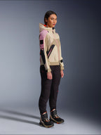 Modelka w kurtce Alpinestars Molly Air Jacket w kolorze Sand Pink Almond, zestawiona z ciemnymi spodniami technicznymi i wysokimi butami motocyklowymi, miejska kurtka motocyklowa z kapturem i wielokolorowymi panelami, nowoczesny design inspirowany stylem streetwear